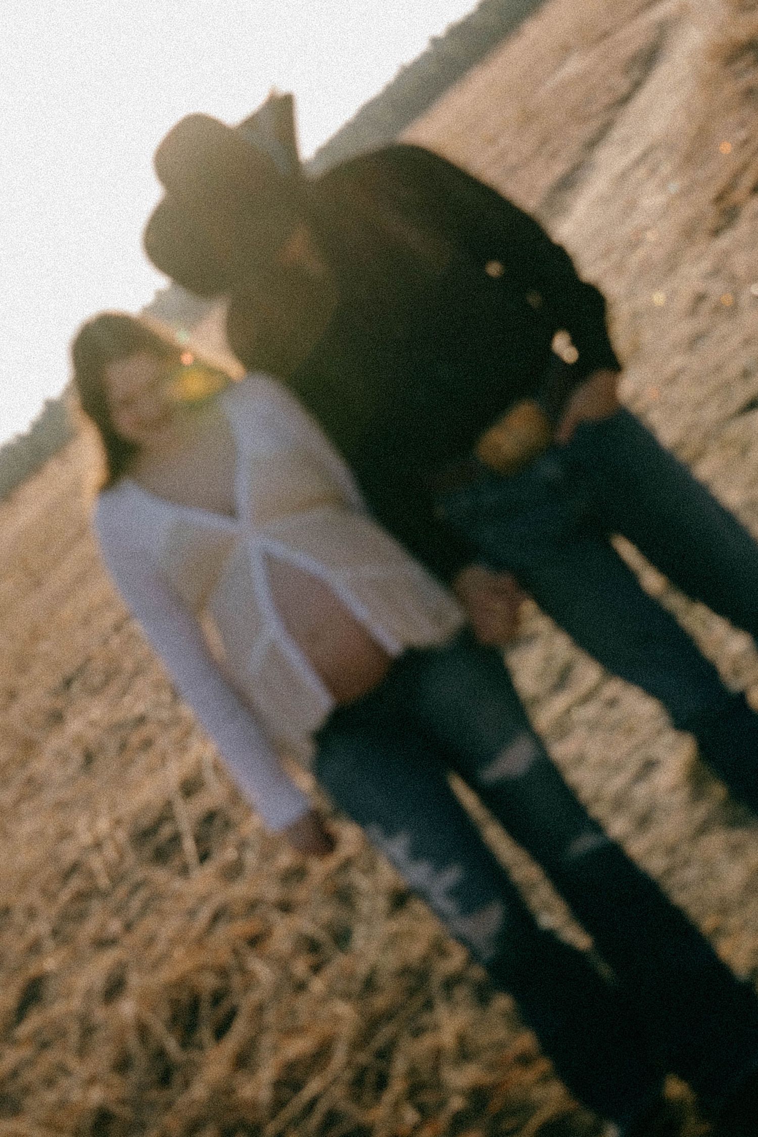 Blurry artistic photo of a pregnant couple standing in a golden field at sunset.