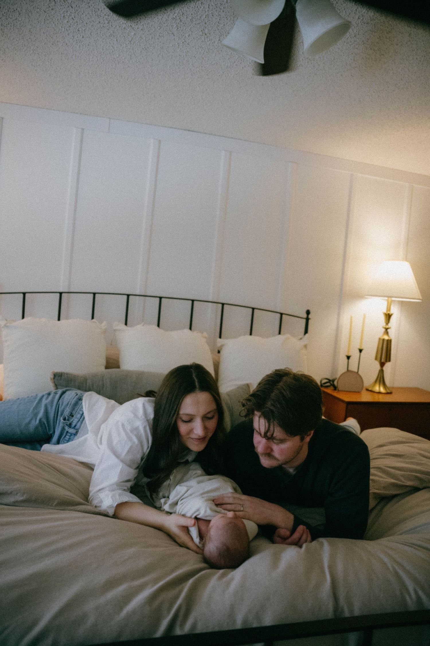 New parents lying on bed together, gazing lovingly at their newborn baby.
