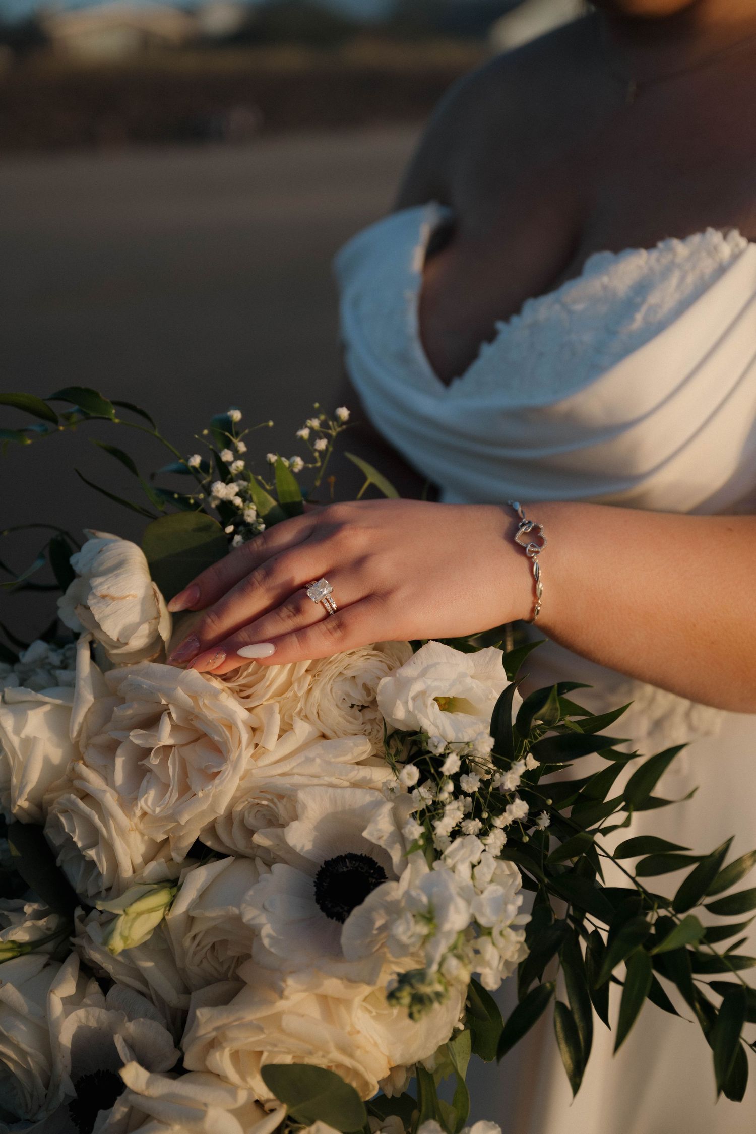 Close-up of a bride's hand adorned with a diamond ring and bracelet resting on a white floral bouquet.