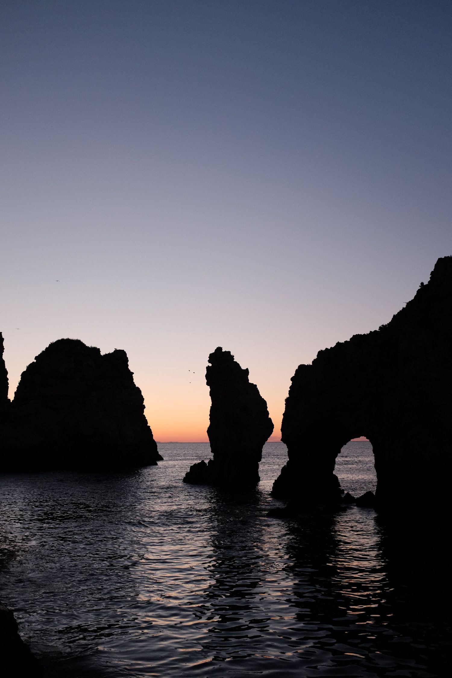 Dramatic silhouette of rocky sea arches at Ponta da Piedade during golden sunset in Lagos Portugal.