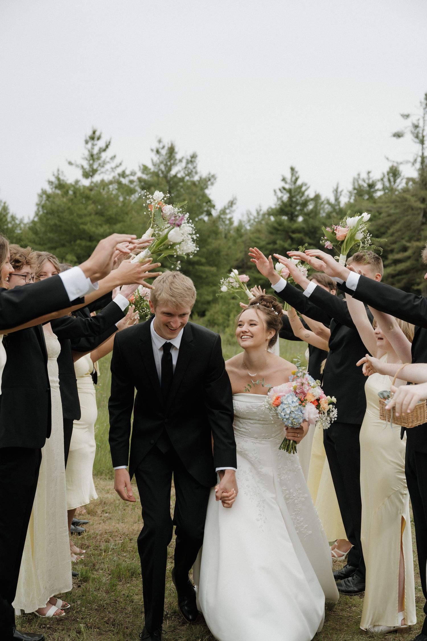 Bride and groom walk through arch of raised bouquets with wedding party.
