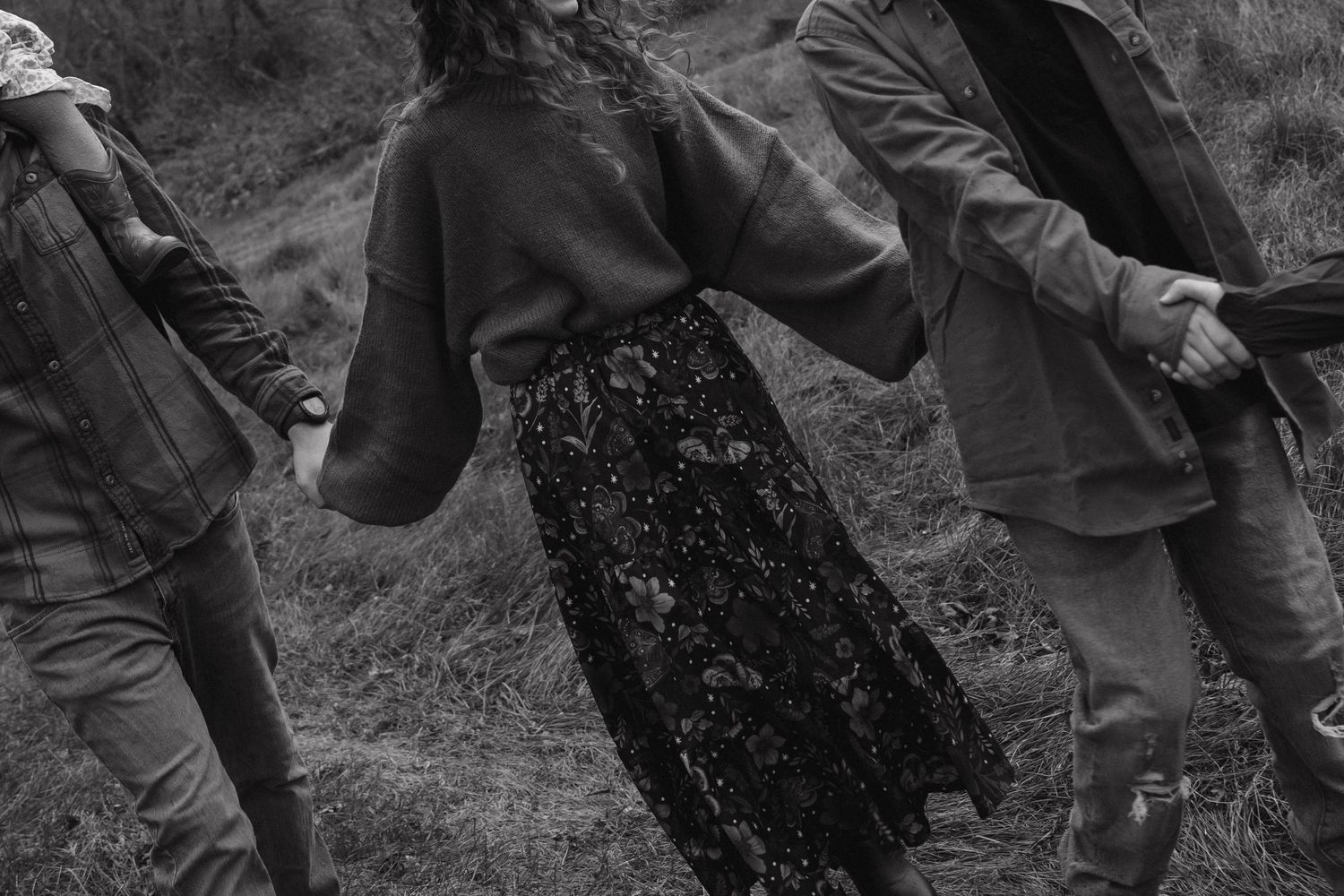 Three people hold hands walking through misty fields, black and white portrait.
