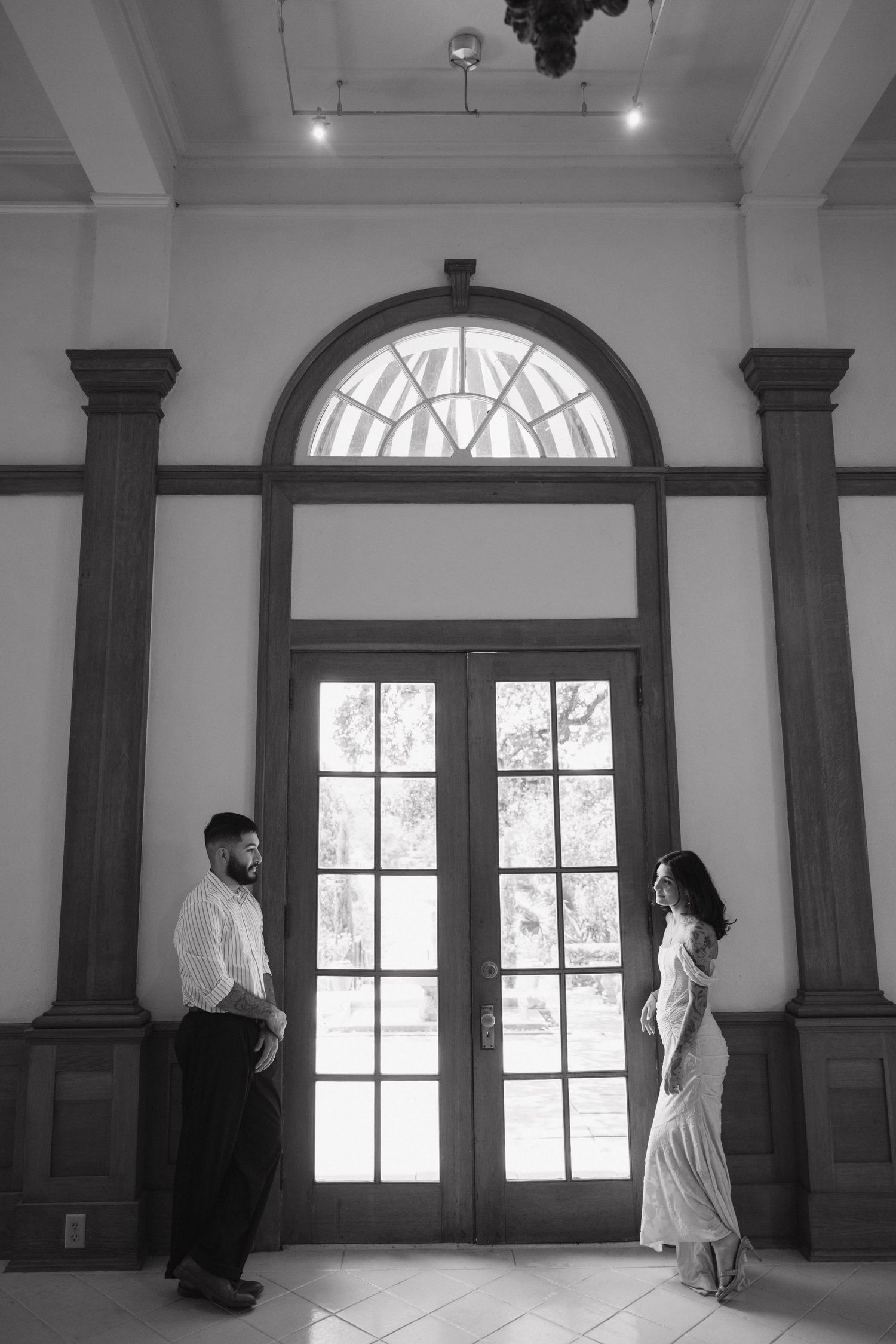 Black and white photo of a couple standing facing each other before elegant arched French doors.