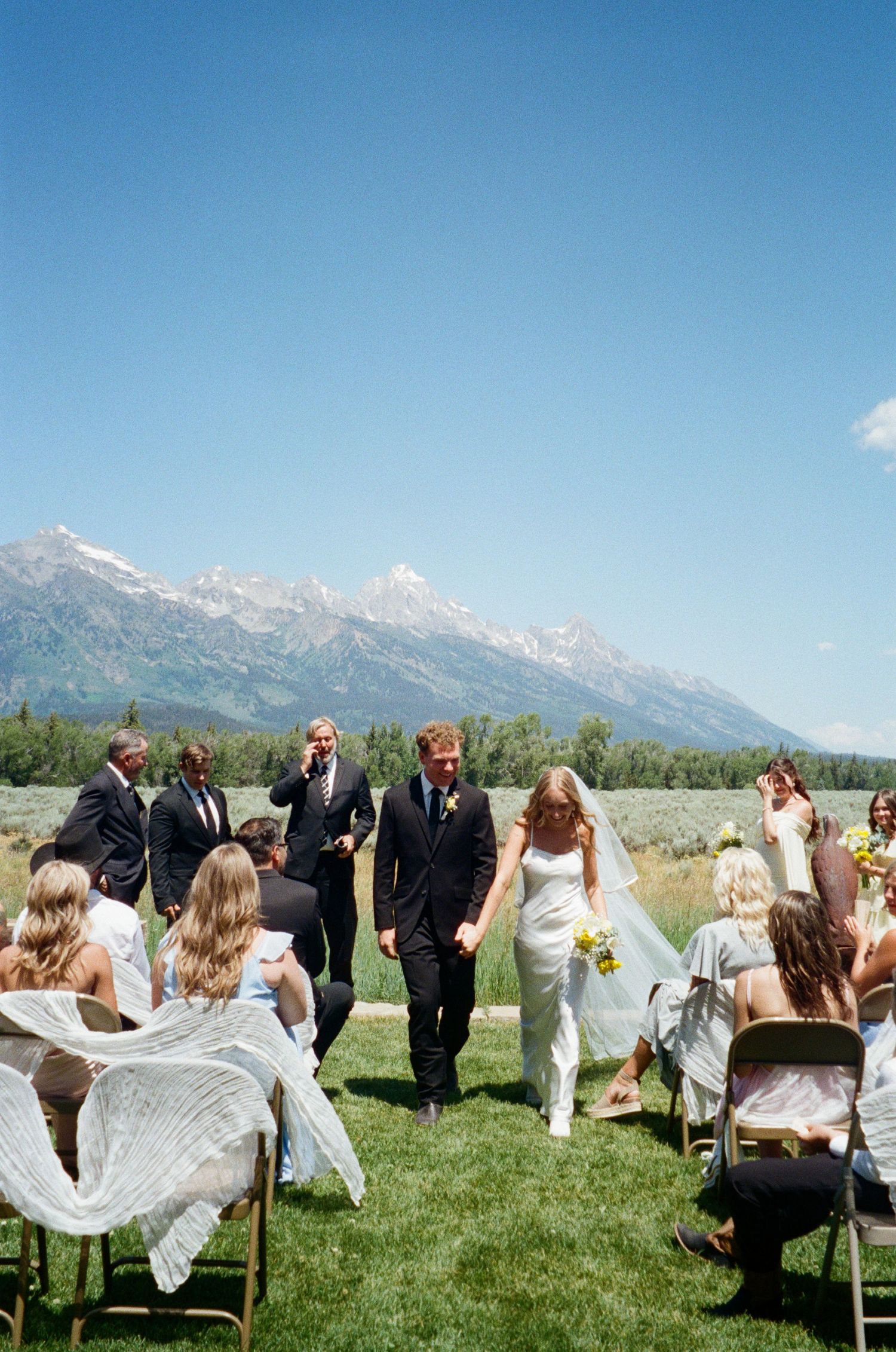 Bride and groom walk down the aisle after ceremony with stunning Grand Teton mountain range in the background.