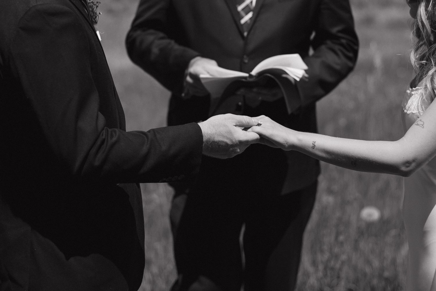 Black and white close-up of bride and groom exchanging hands during wedding ceremony.