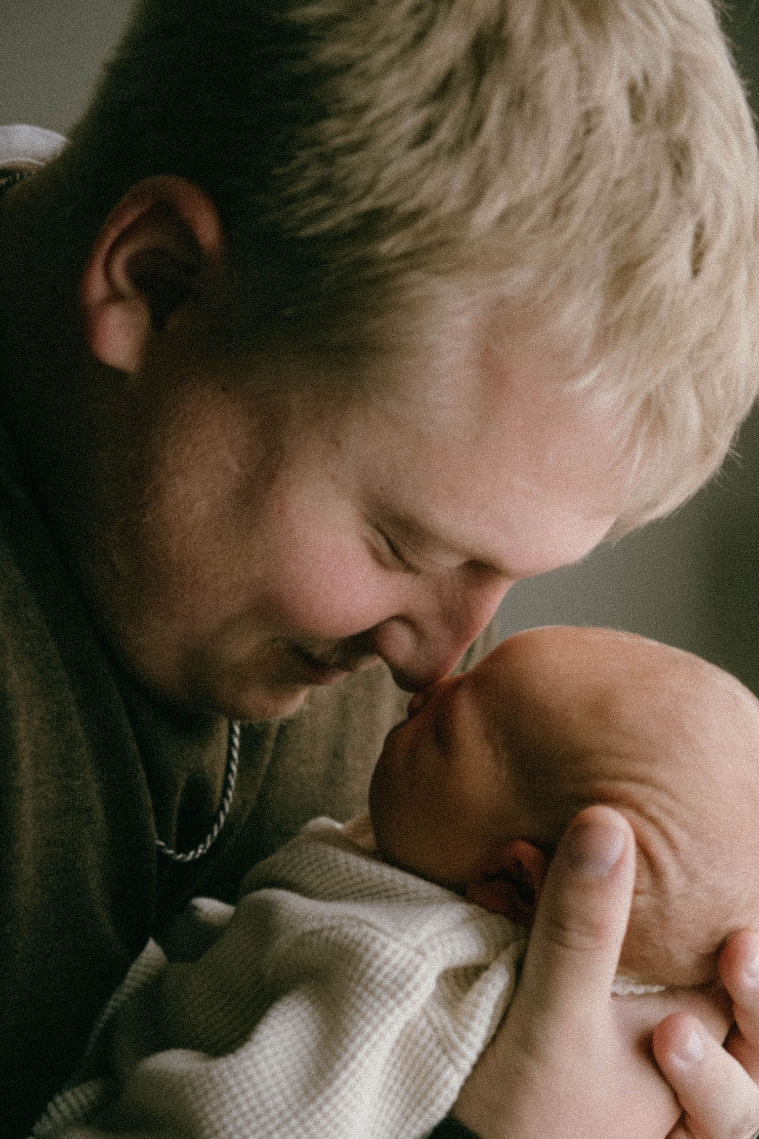 Blond father tenderly kissing his sleeping newborn baby wrapped in white blanket.