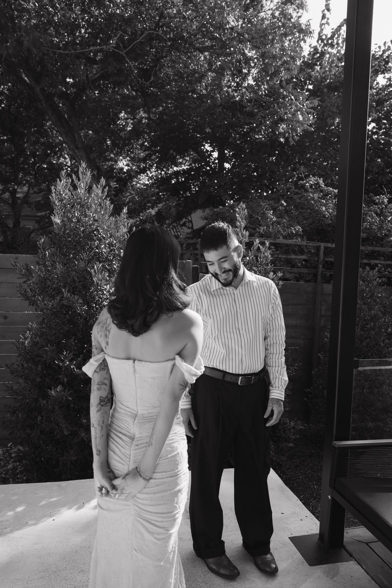 Black and white photo of groom smiling at bride in wedding dress during first look outdoors.