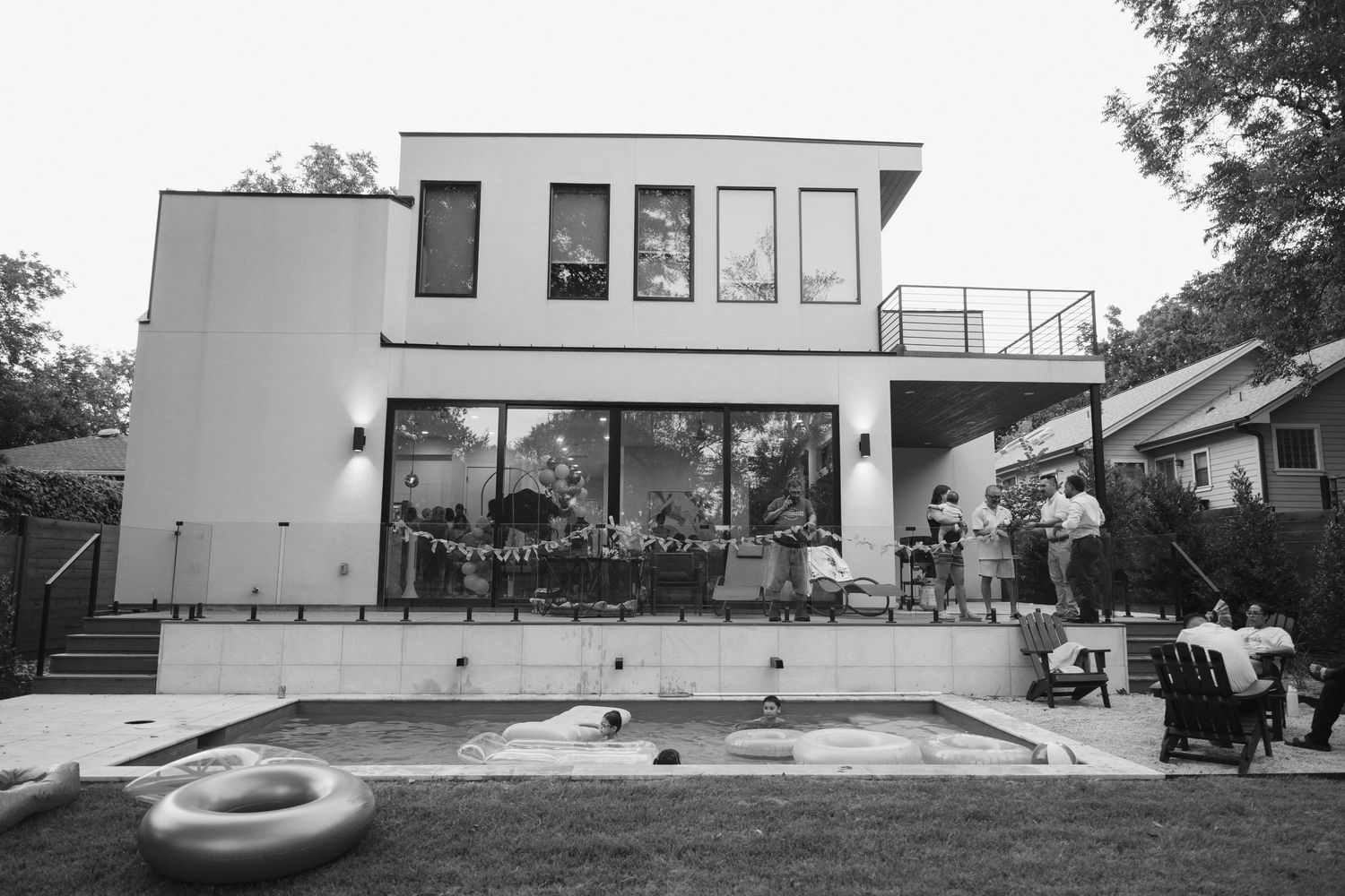 Black and white photo of a modern home with pool during an outdoor wedding reception at dusk.