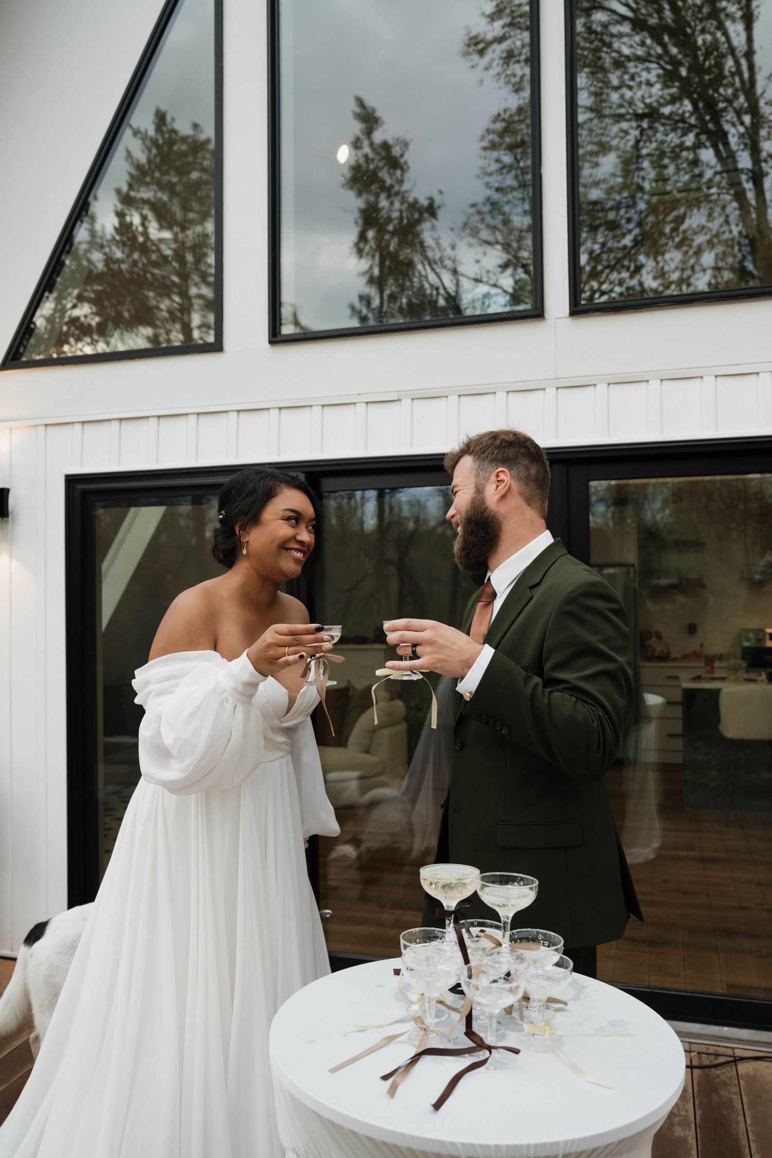 Interracial couple toasting champagne at wedding reception outside modern white building.