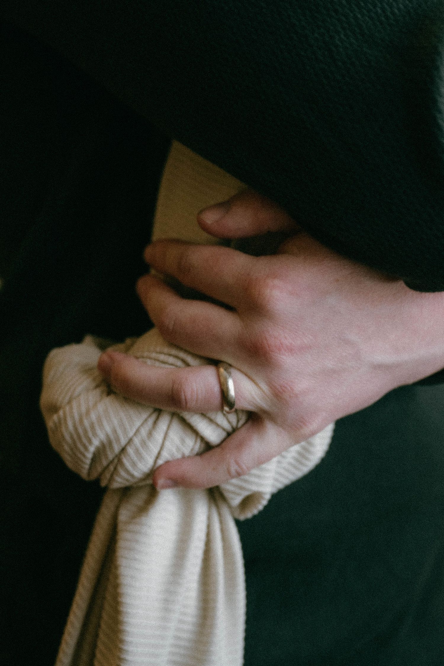 Close-up of fathers hand wearing gold wedding band gently holding newborn baby.