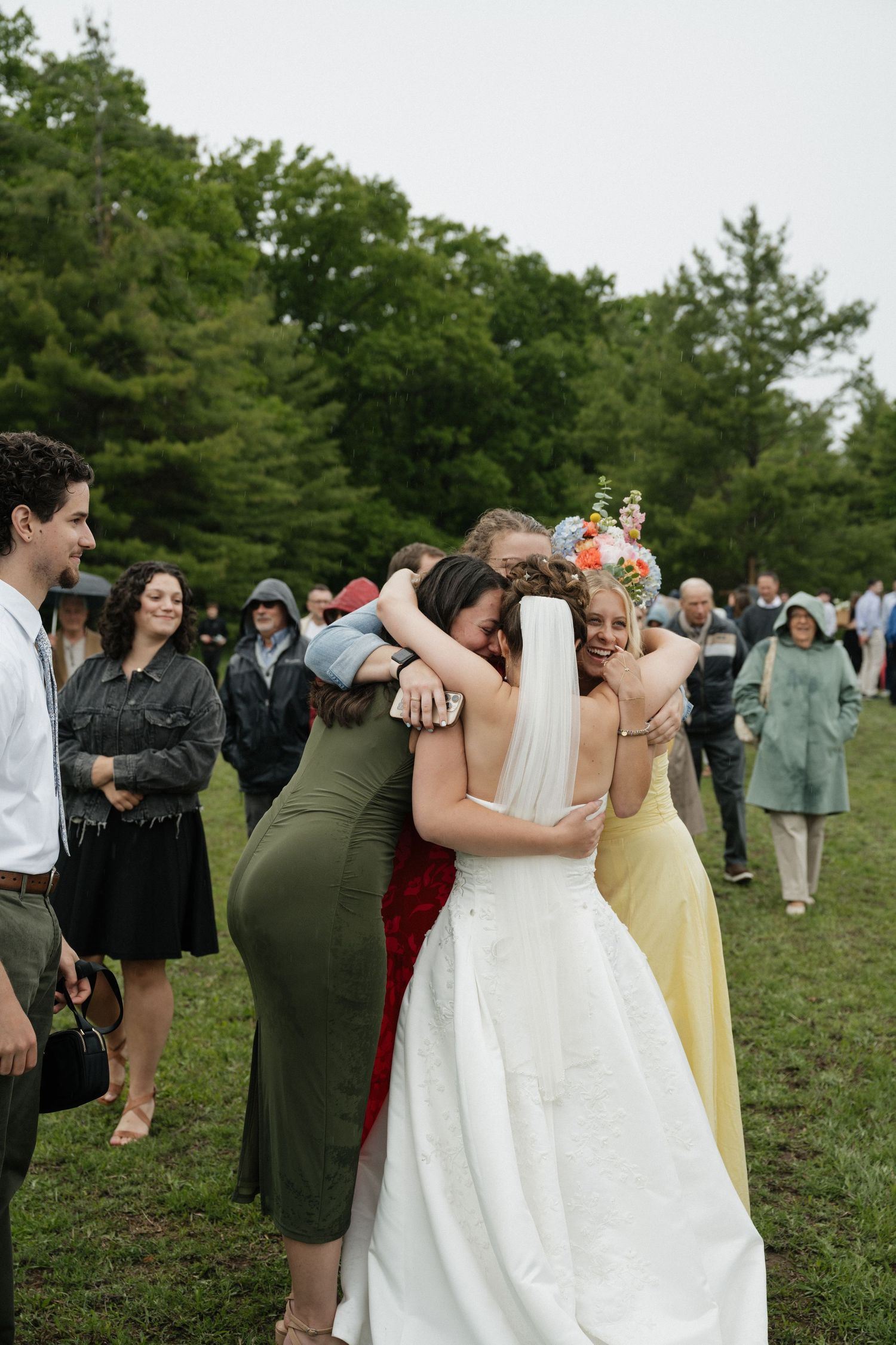 Bride in white dress receives hugs from guests at outdoor wedding.