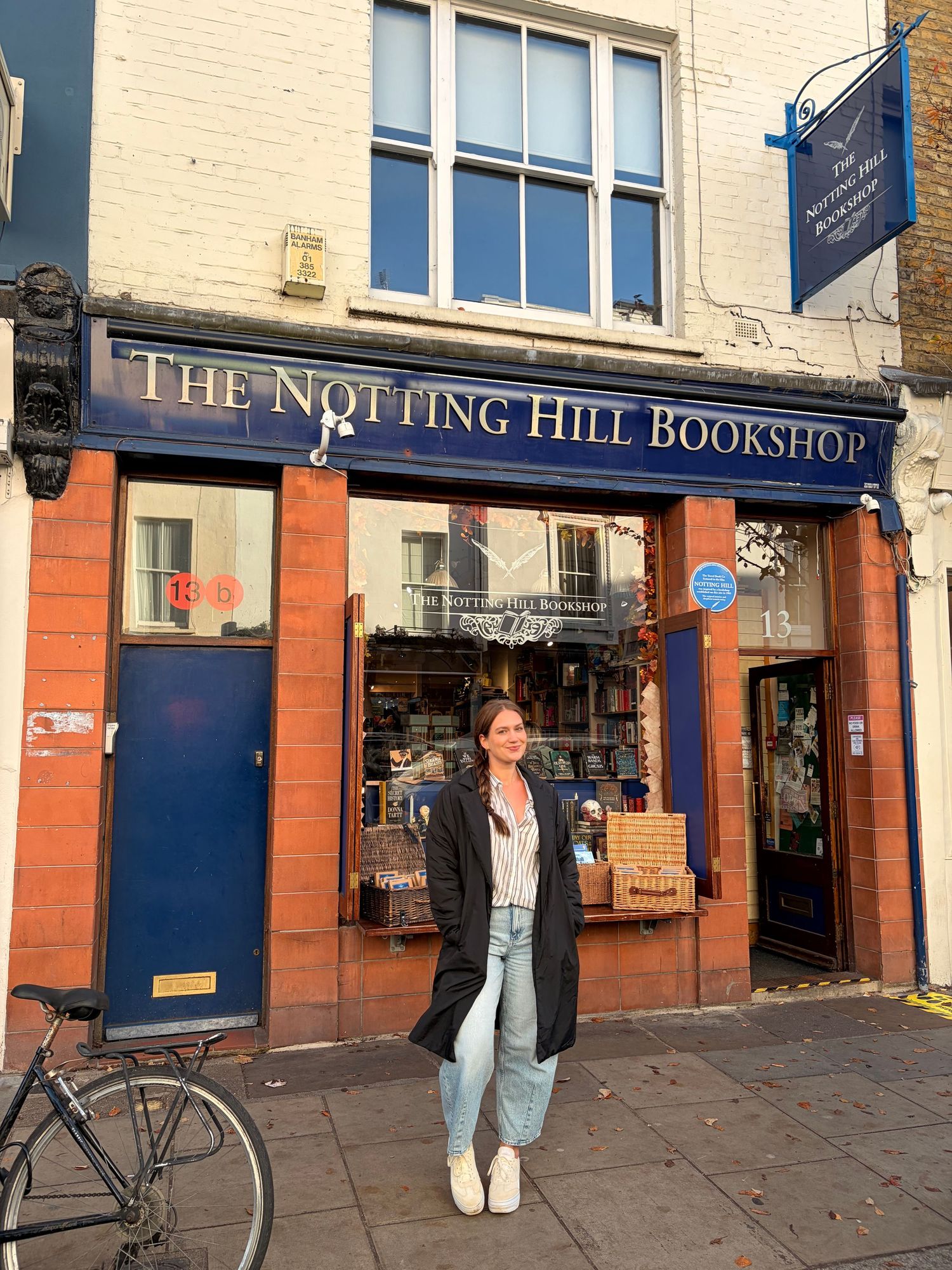 Woman smiling outside The Notting Hill Bookshop in London on a sunny day.