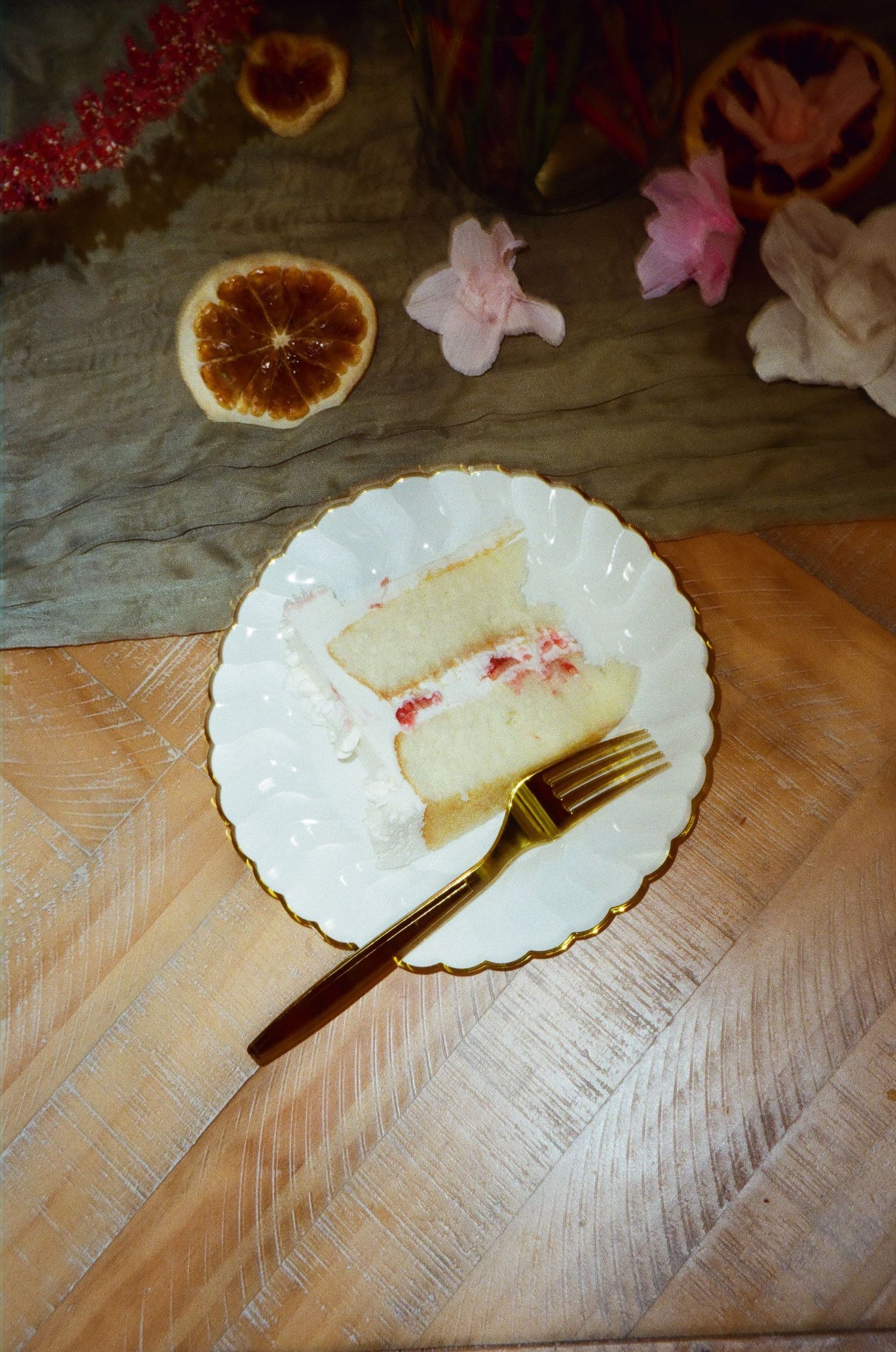 Elegant slice of white wedding cake on gold-rimmed plate with gold fork on wooden table.