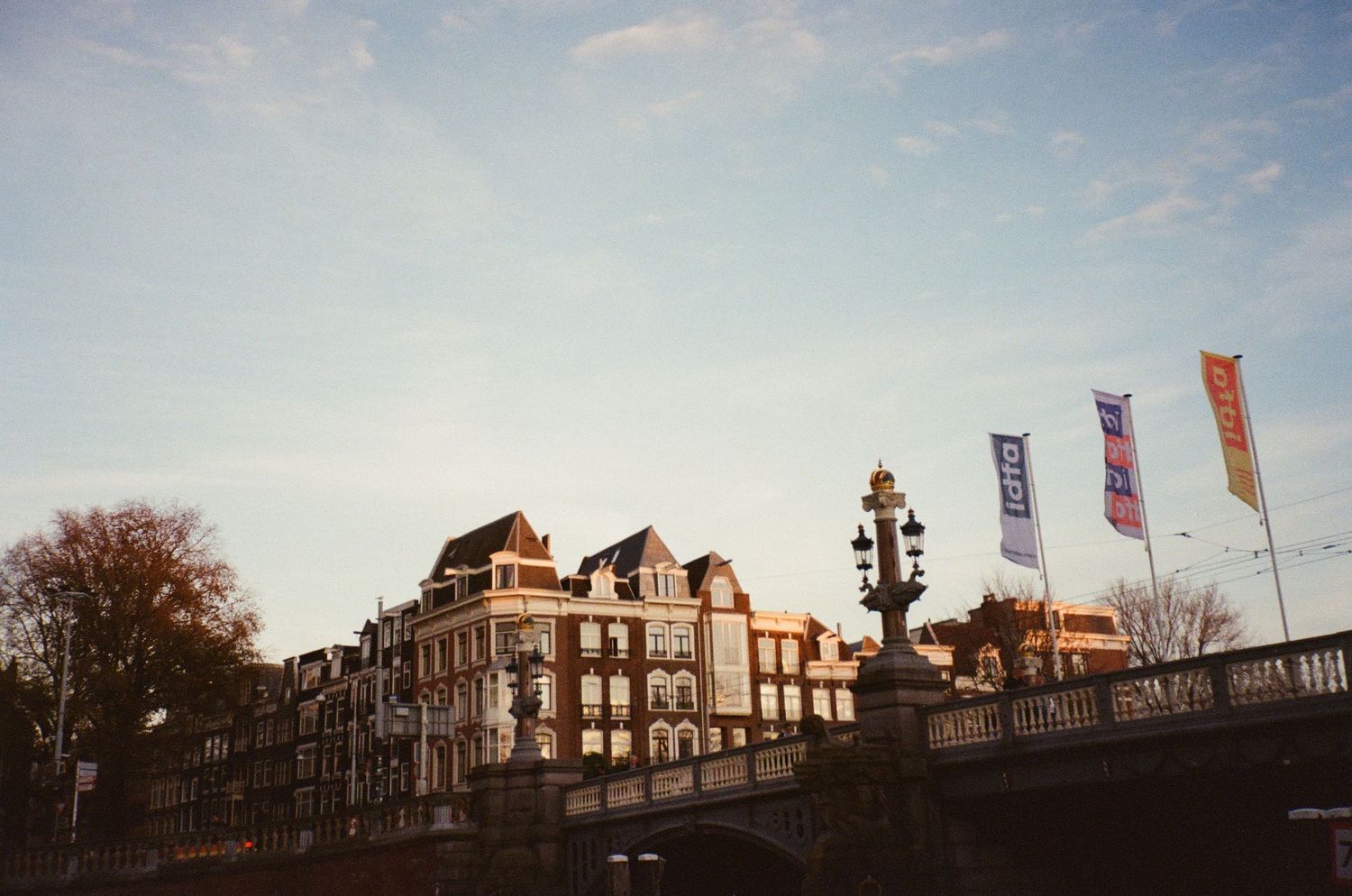 Historic Amsterdam canal bridge at sunset with colorful flags and traditional Dutch architecture.