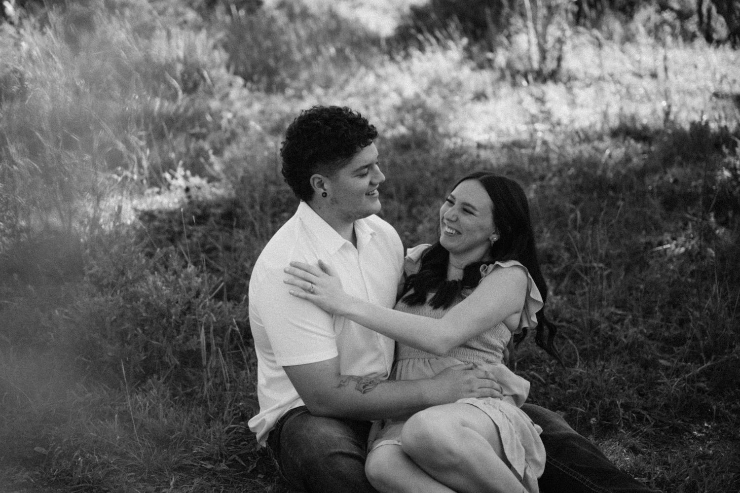 Black and white romantic couple sitting in meadow grass, smiling and embracing each other.