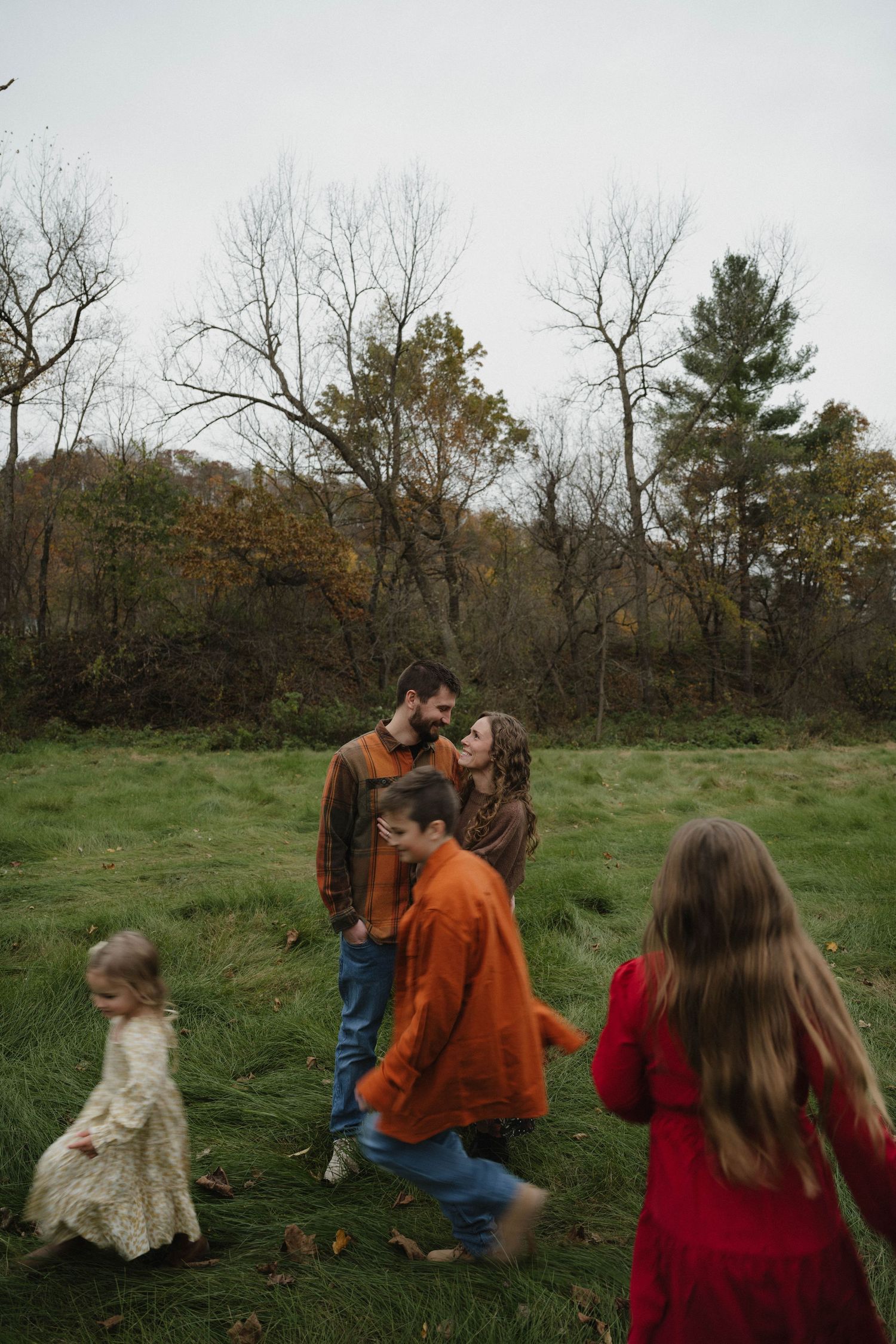A couple sharing a tender moment while their three children play around them in a green meadow.