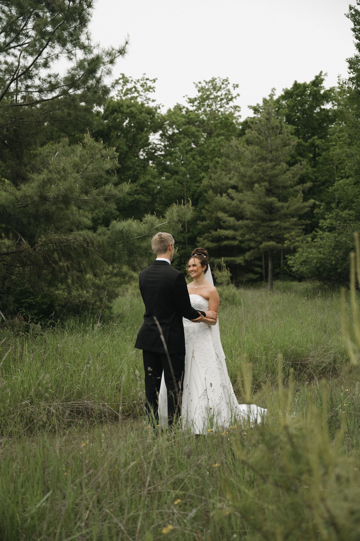 Bride and groom sharing a romantic moment in a lush green meadow surrounded by tall trees.
