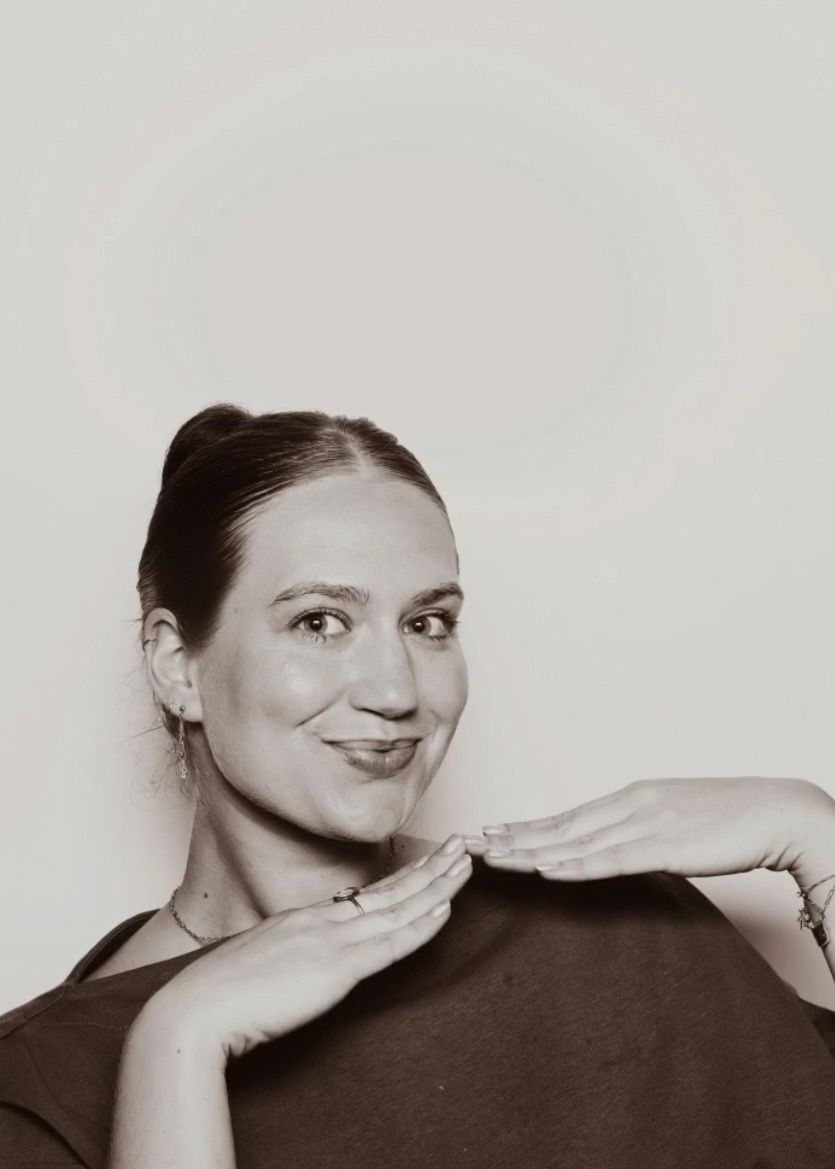 Black and white portrait of smiling woman with hair up, hands gracefully posed near chin.
