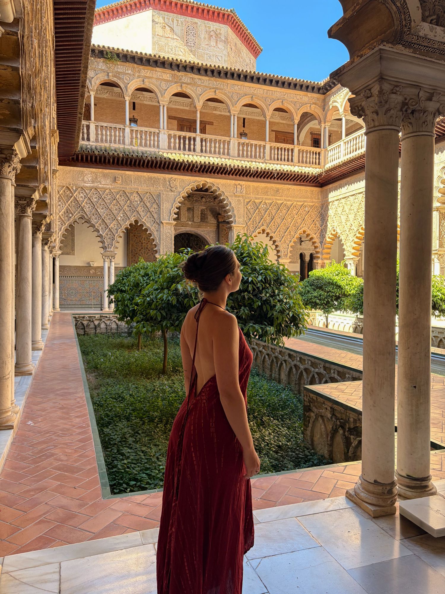 Woman in red backless dress admiring ornate Moorish architecture at Real Alcazar palace in Seville Spain.