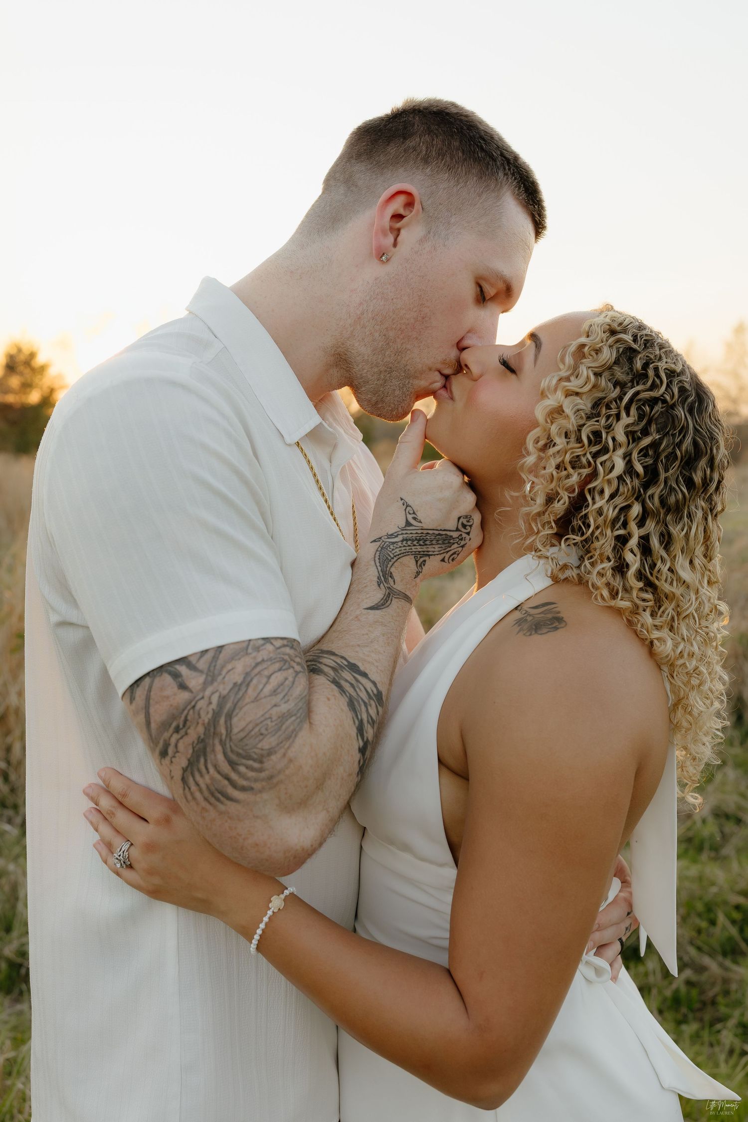 Couple sharing a kiss in golden field at sunset.
