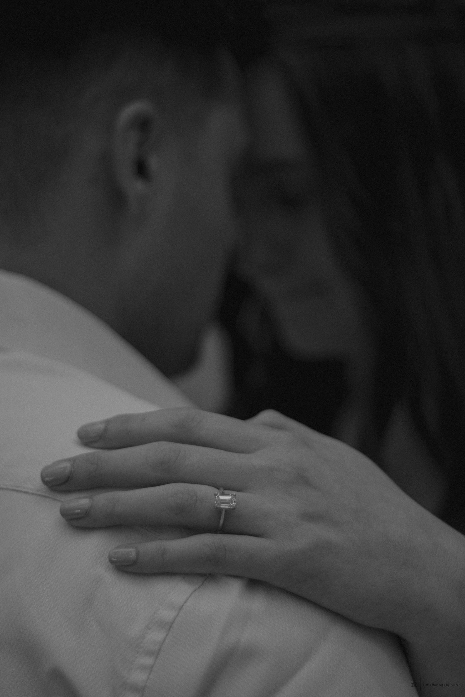 Black and white photo of a couple embracing, woman's hand on man's shoulder showing an engagement ring.