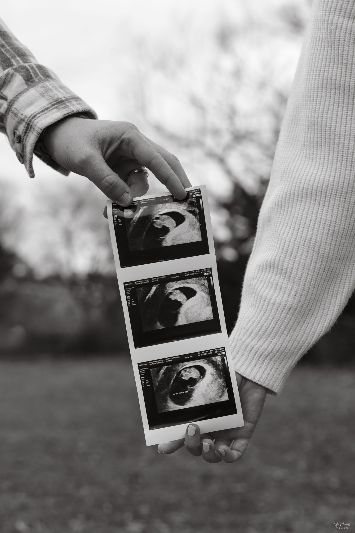 Couple holding ultrasound photos together outdoors in black and white.
