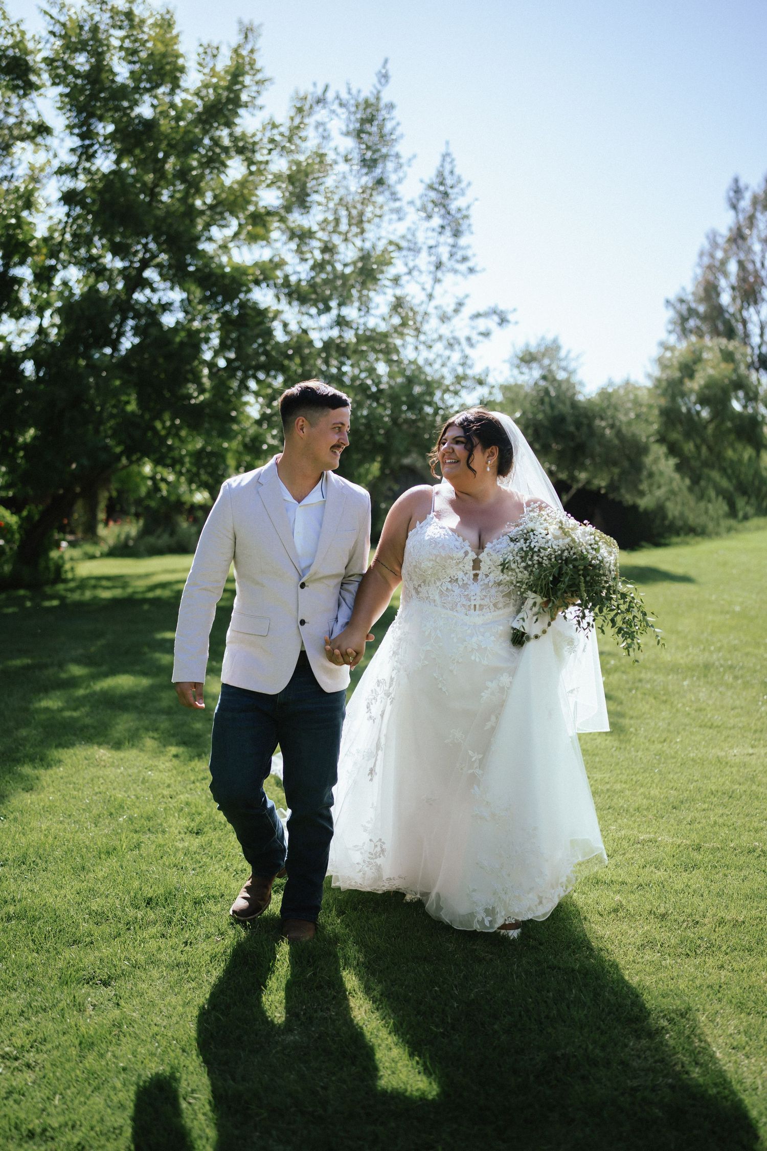 Wedding couple playfully walking and dancing together on a sunny grassy hill.