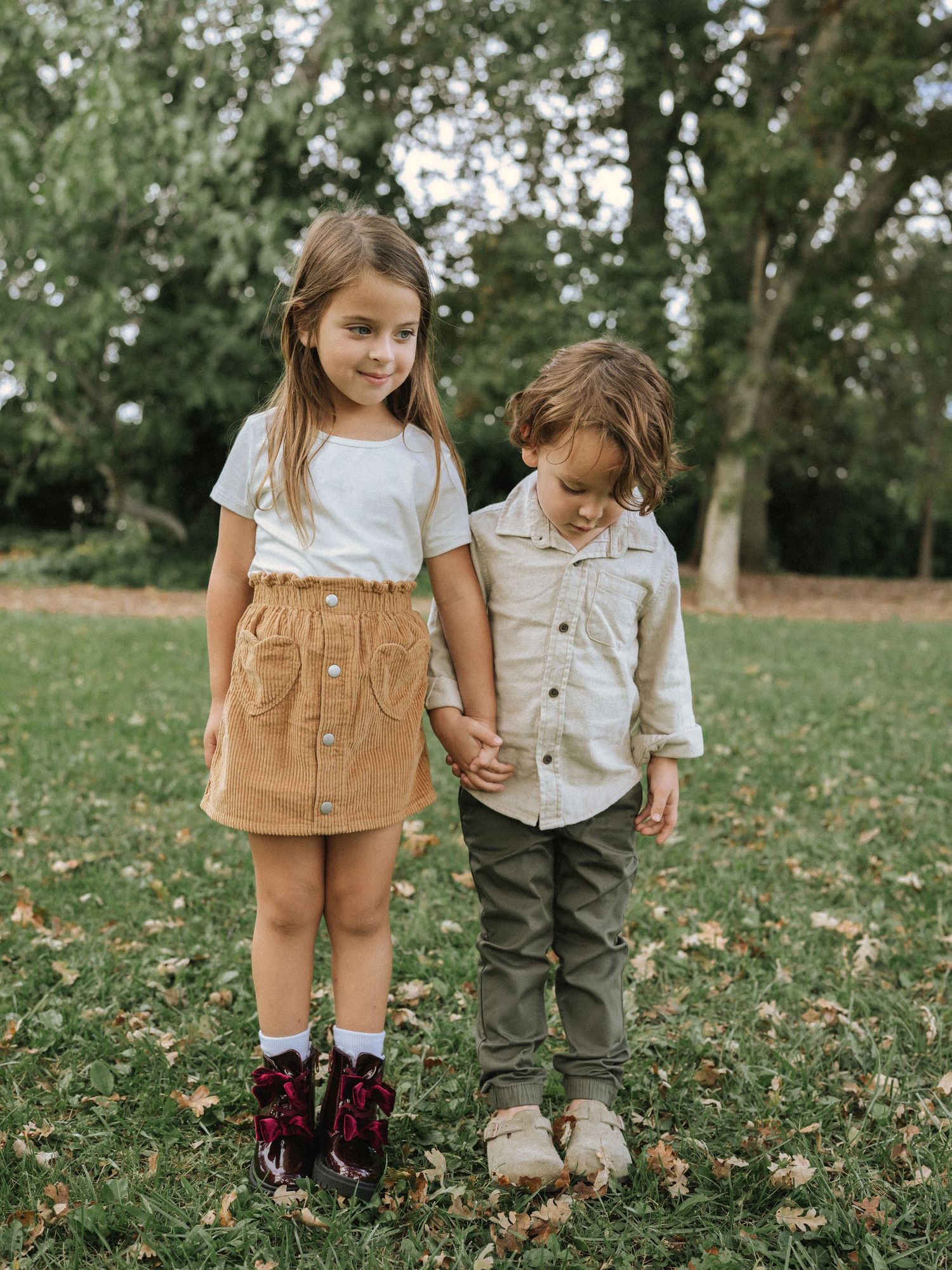 Young children walking together through fallen autumn leaves in casual clothing.