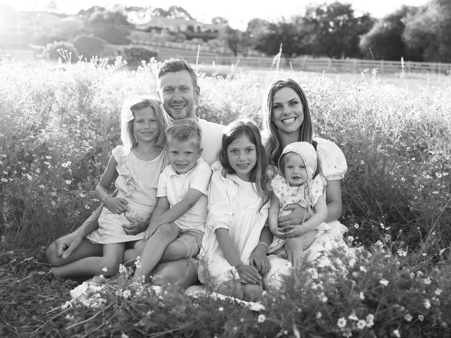 Black and white family portrait of parents with four young children sitting in a wildflower field.