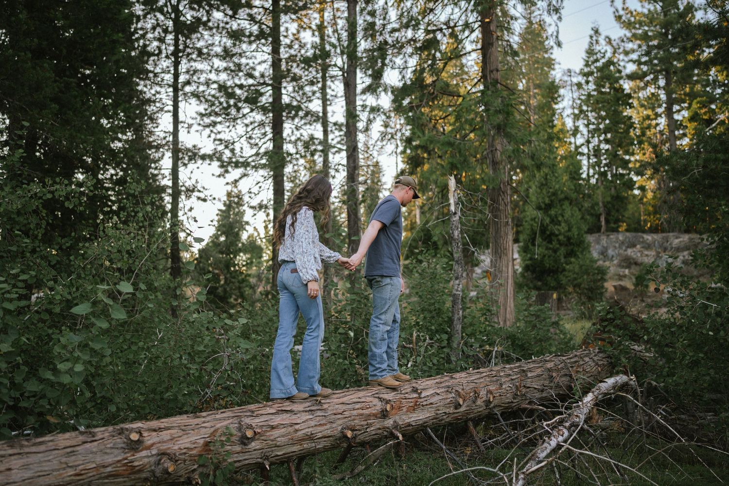Couple walking together on fallen logs in a peaceful forest setting.