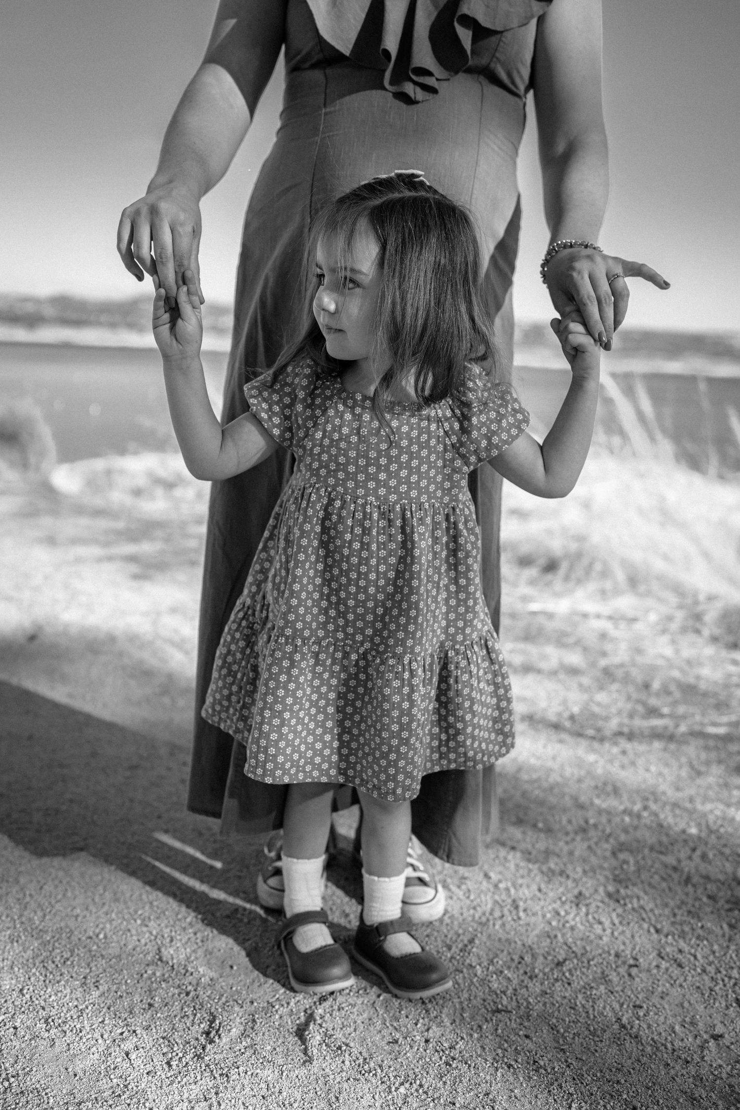 Black and white image of small feet in polka dot dress and shoes on textured ground.