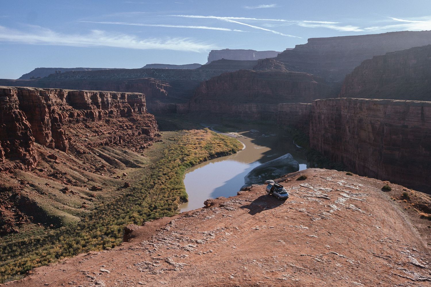 Panoramic views of a winding river cutting through red rock canyons and cliffs in a desert landscape.