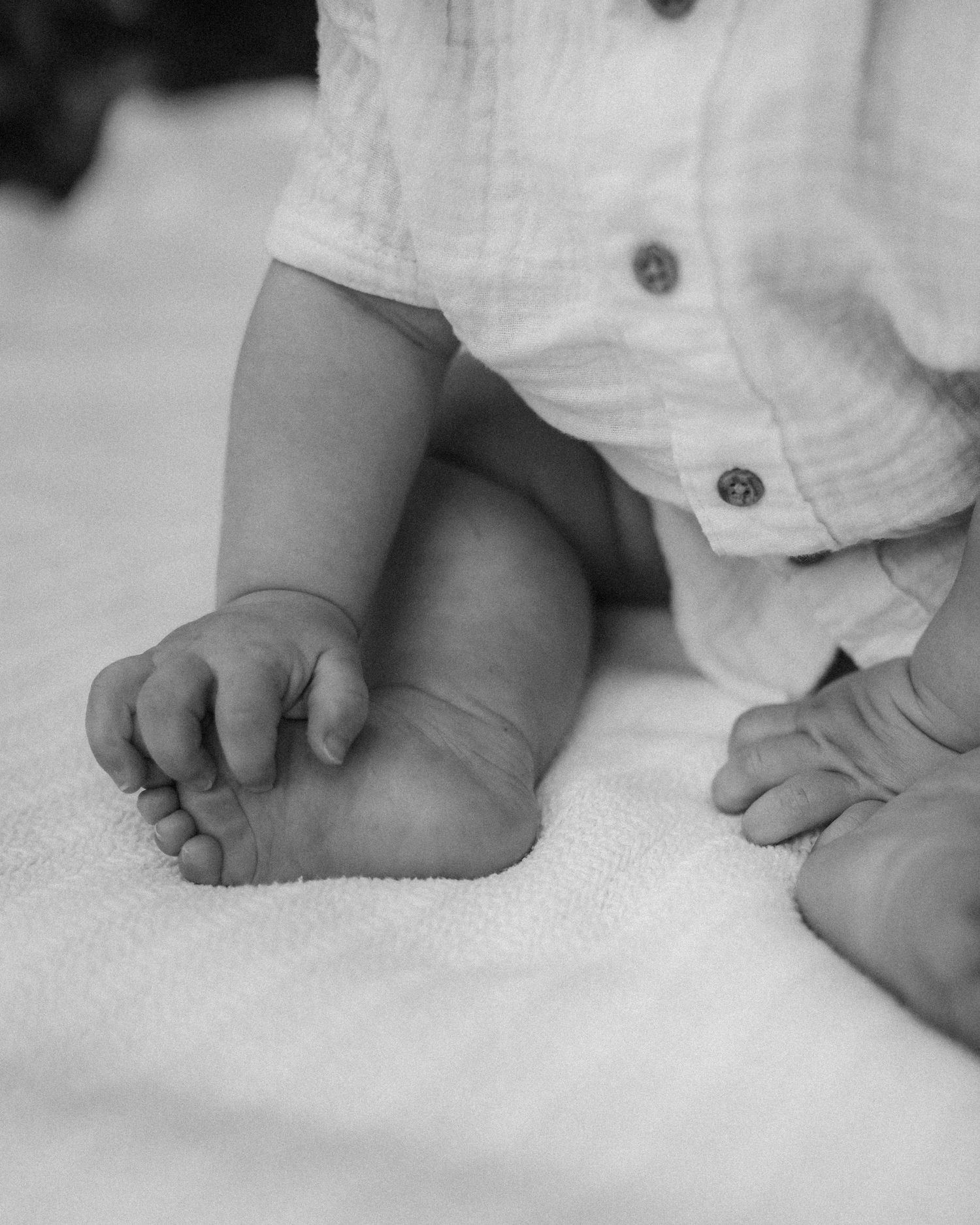 Black and white close-up of tiny baby feet on white fabric.