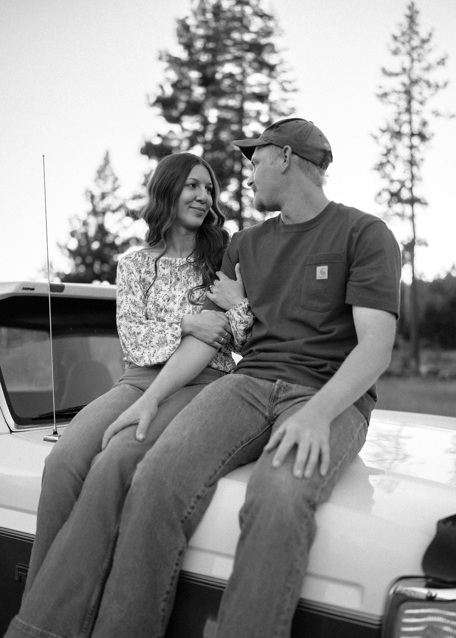 Couple sitting on the tailgate of a pickup truck in a forest setting.