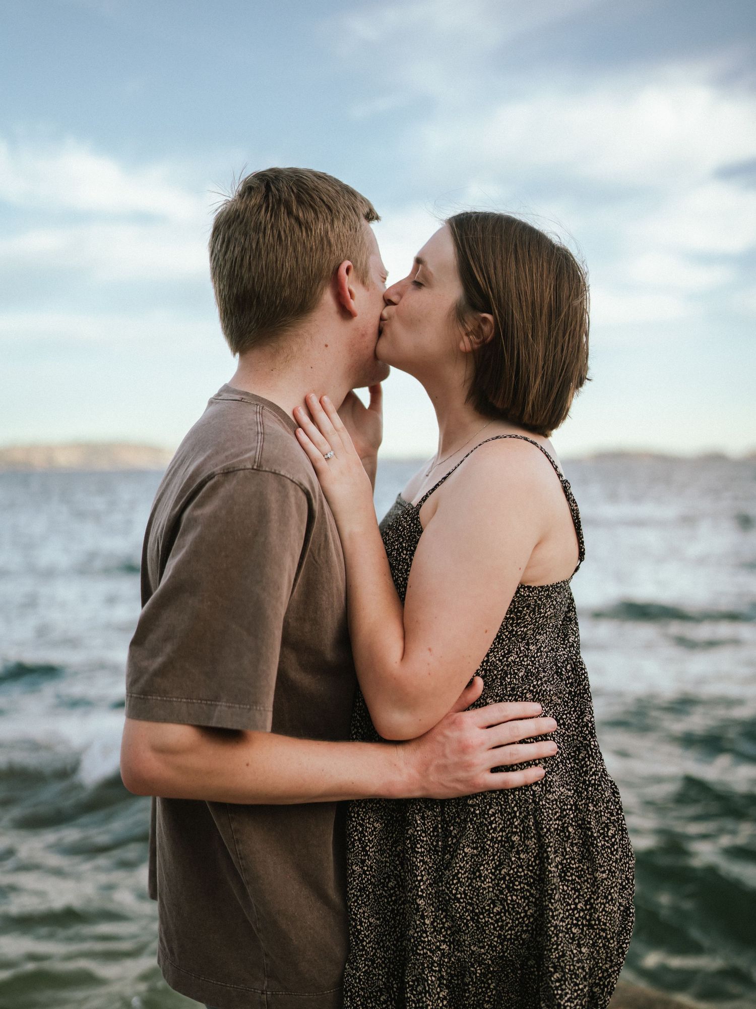 Romantic couple sharing kisses against an ocean backdrop at sunset.