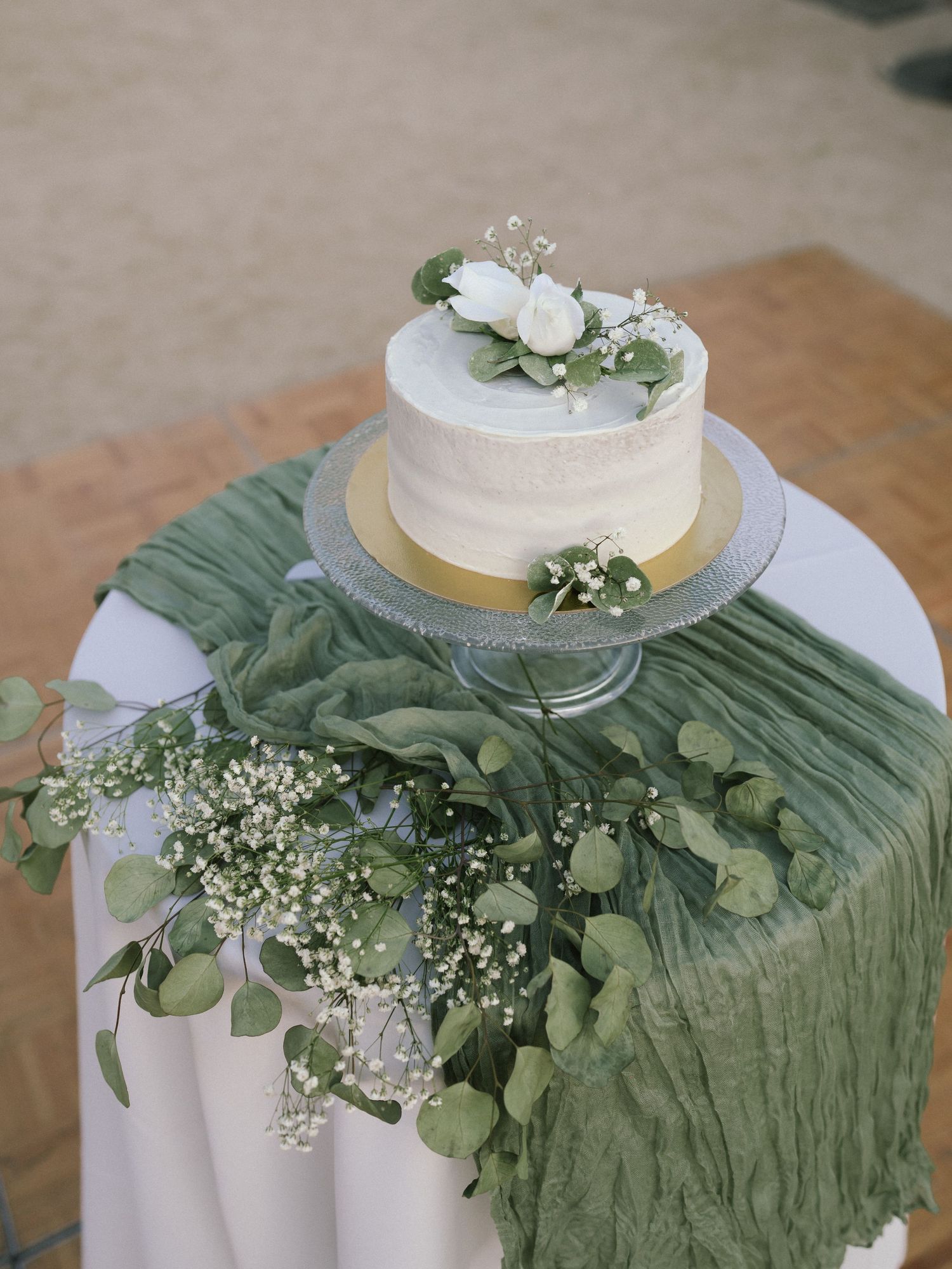 Wedding cake display with sage green runner and delicate baby's breath floral decorations.