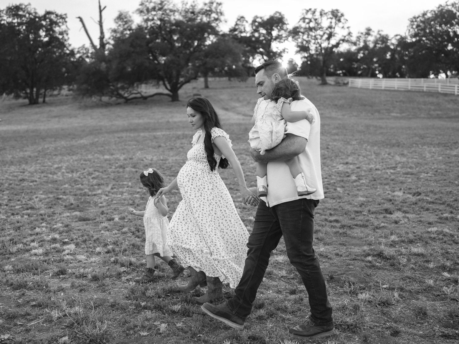 Black and white photo of a family walking in a field, parents holding children in a candid outdoor portrait.