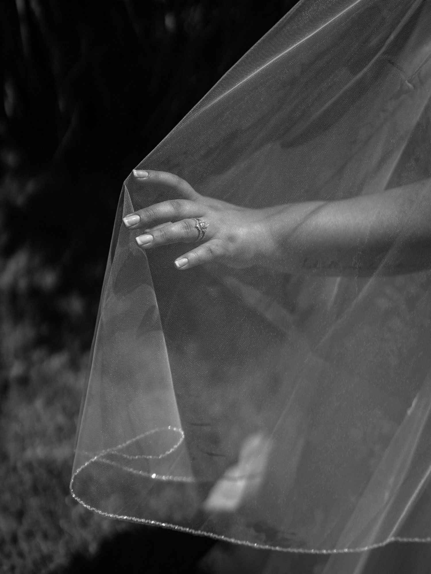 Close-up details of a flowing white wedding veil with delicate lace trim against a dark background.
