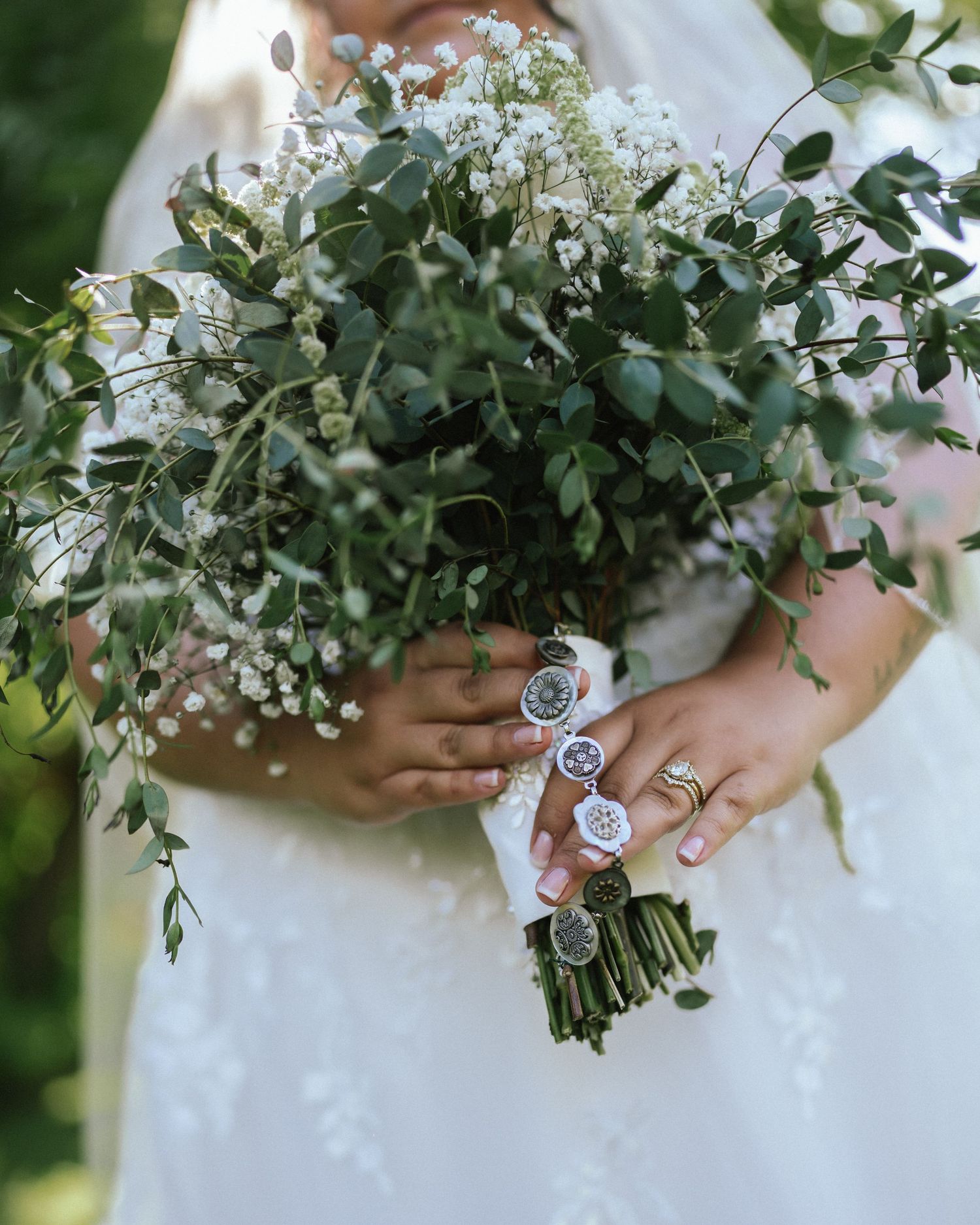 Elegant bridal bouquet with white flowers and green foliage held against a white dress.