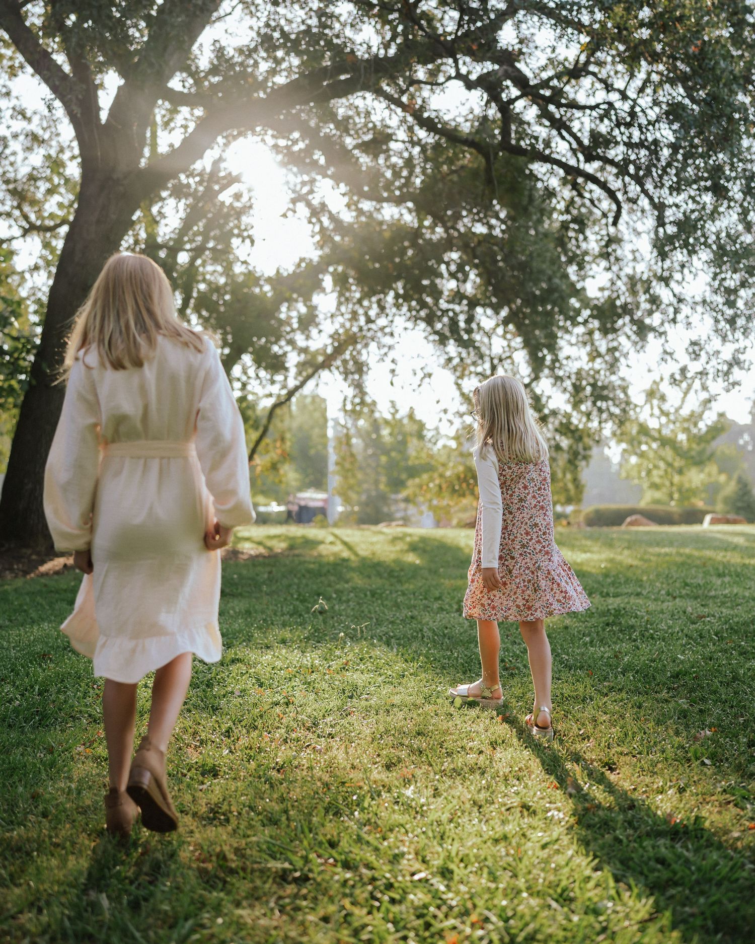 People walking through sunlit grass wearing white and floral dresses.