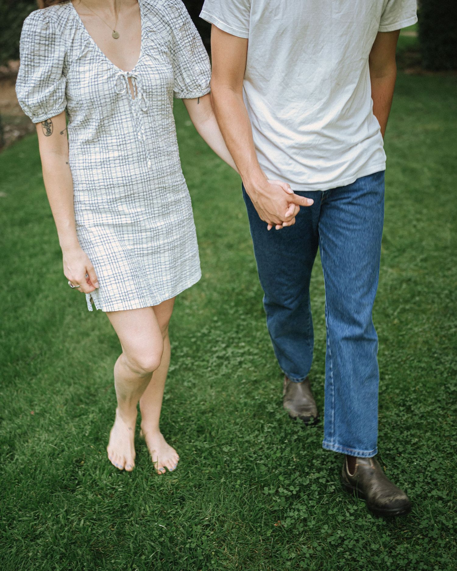 Couple walking barefoot together on green grass in casual summer clothing.