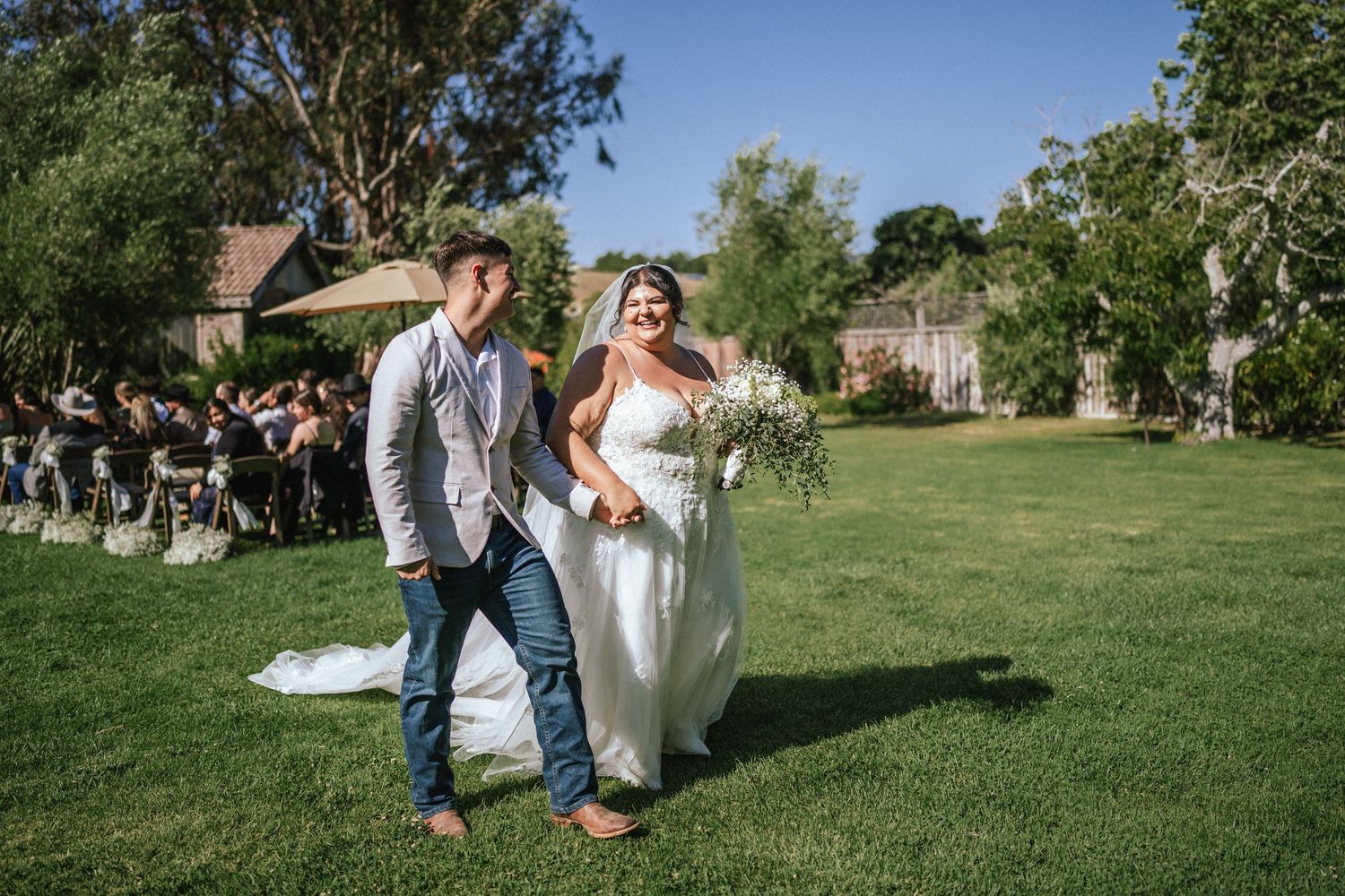 Newlyweds walking together on grass during outdoor wedding ceremony.