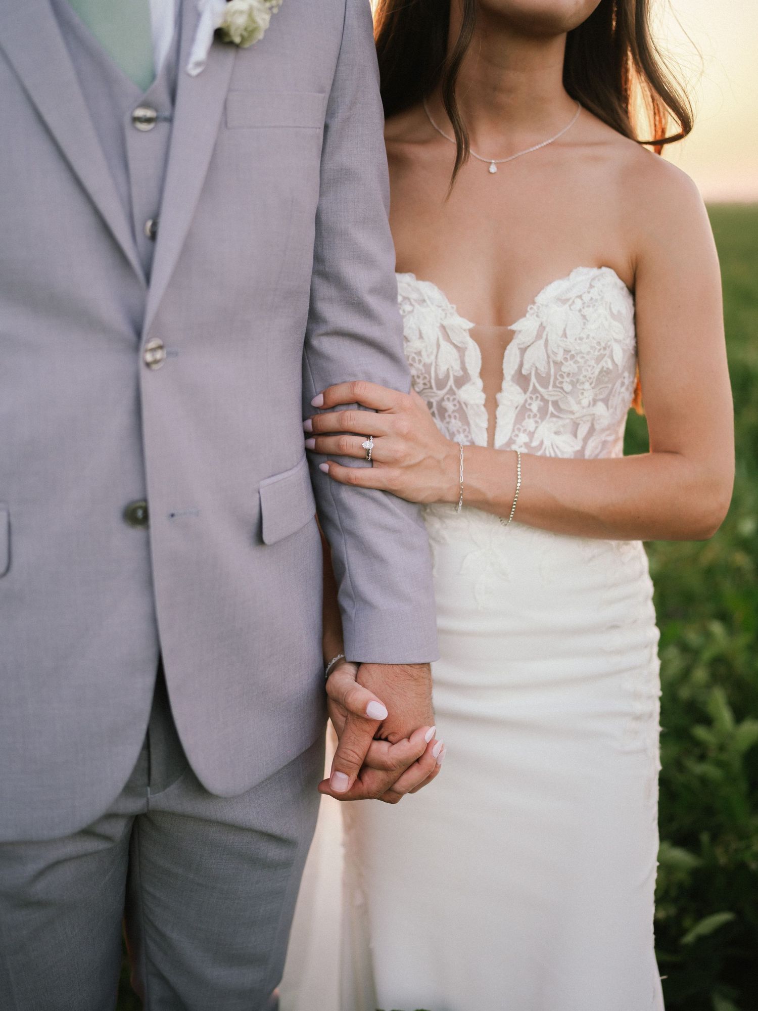 Elegant bride in white dress standing next to groom in light grey suit during outdoor wedding.