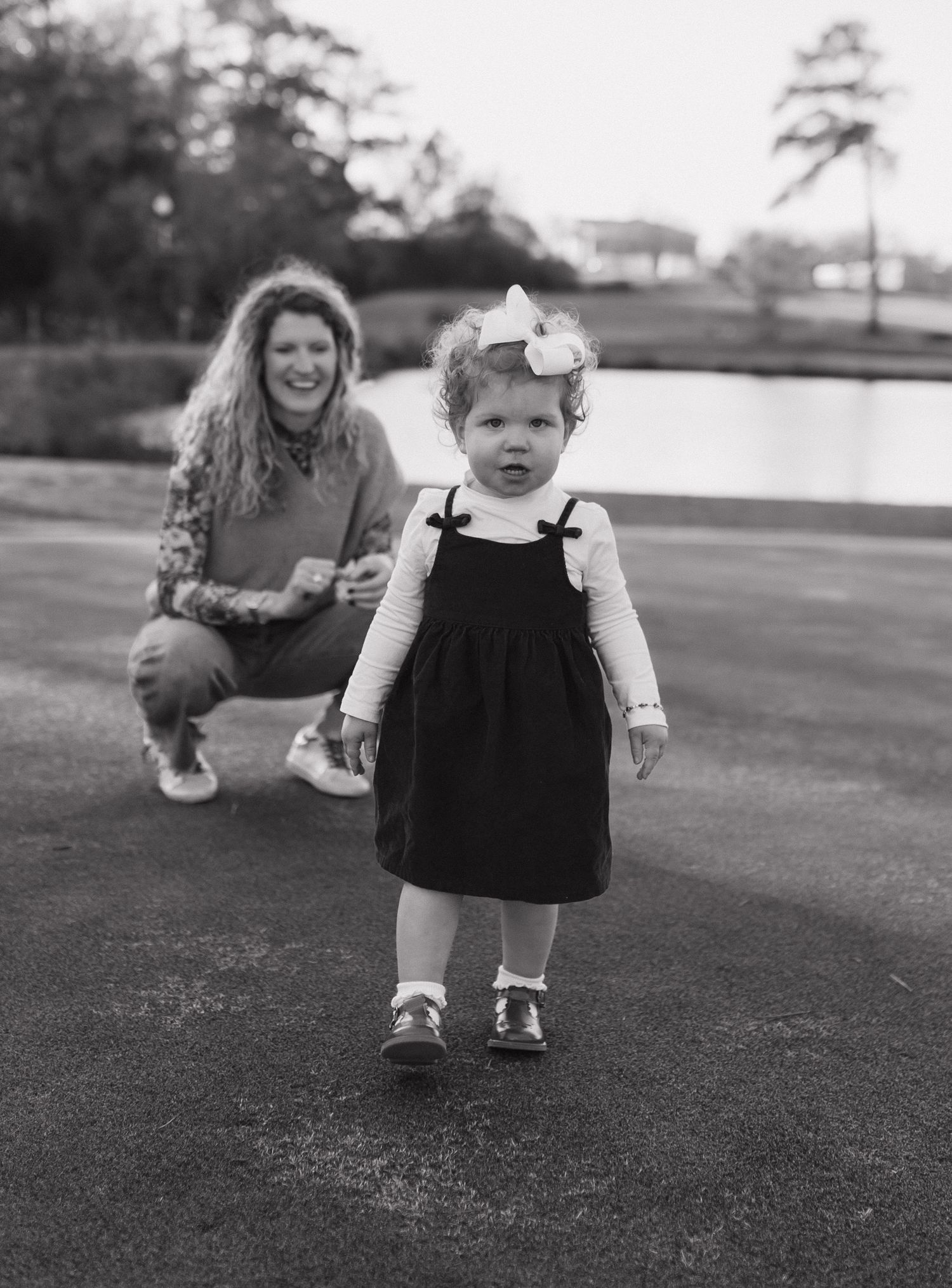 Black and white photo of a small child wearing a dress and bow exploring outdoors. Andalusia, Alabama photographer; South Alabama photograph