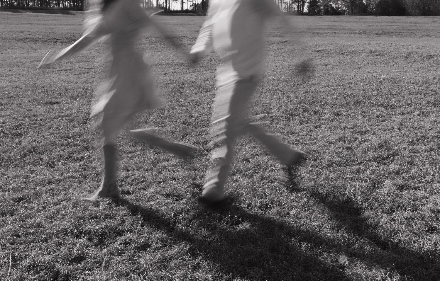 Motion blur captures the dynamic movement of legs and feet running across a grassy field in black and white.