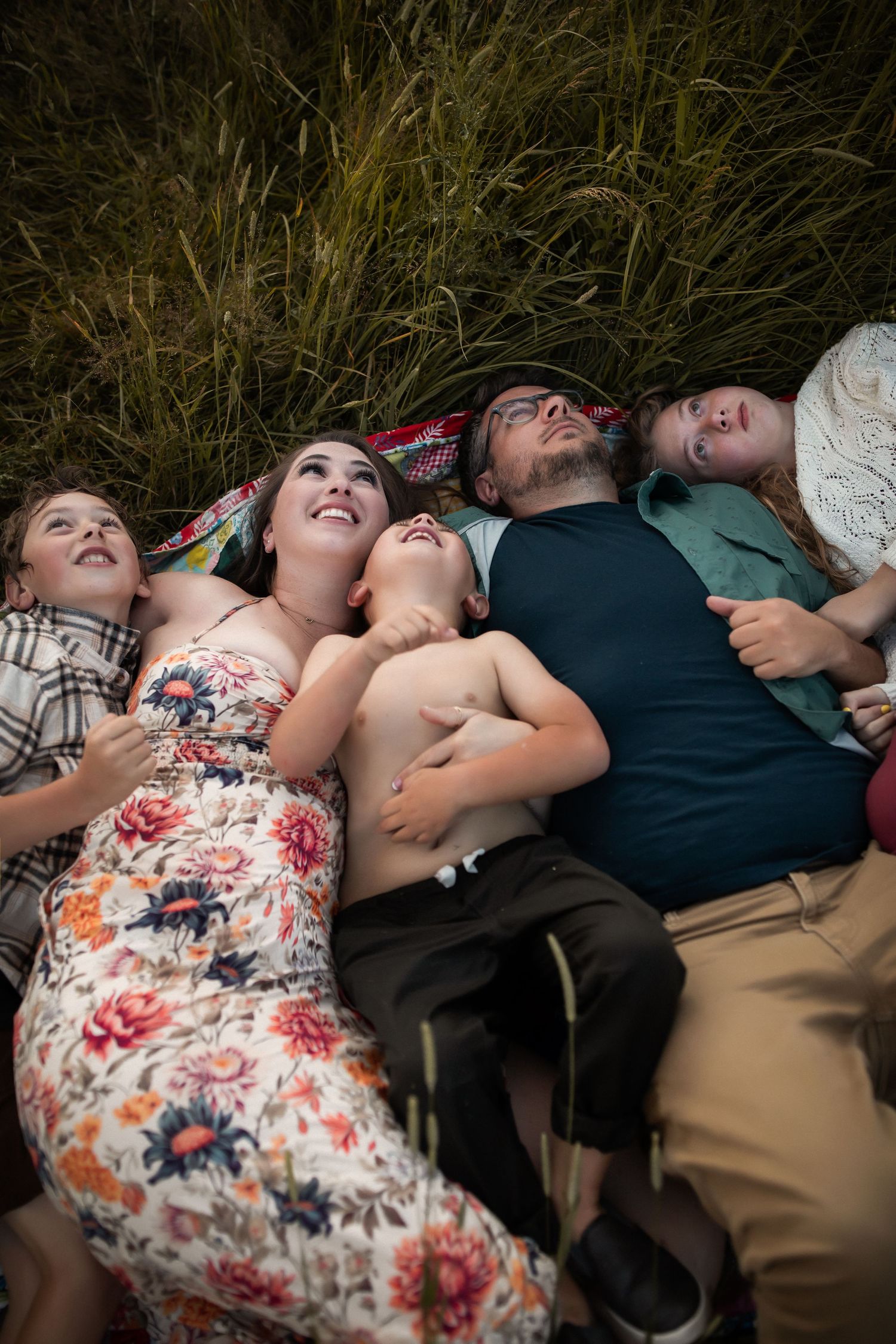 Group lying together on grass looking up at sky during outdoor photo session.