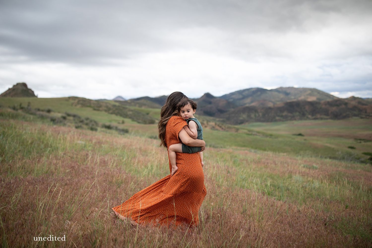 Dramatic mountain landscape with flowing orange dress in wild grass field.