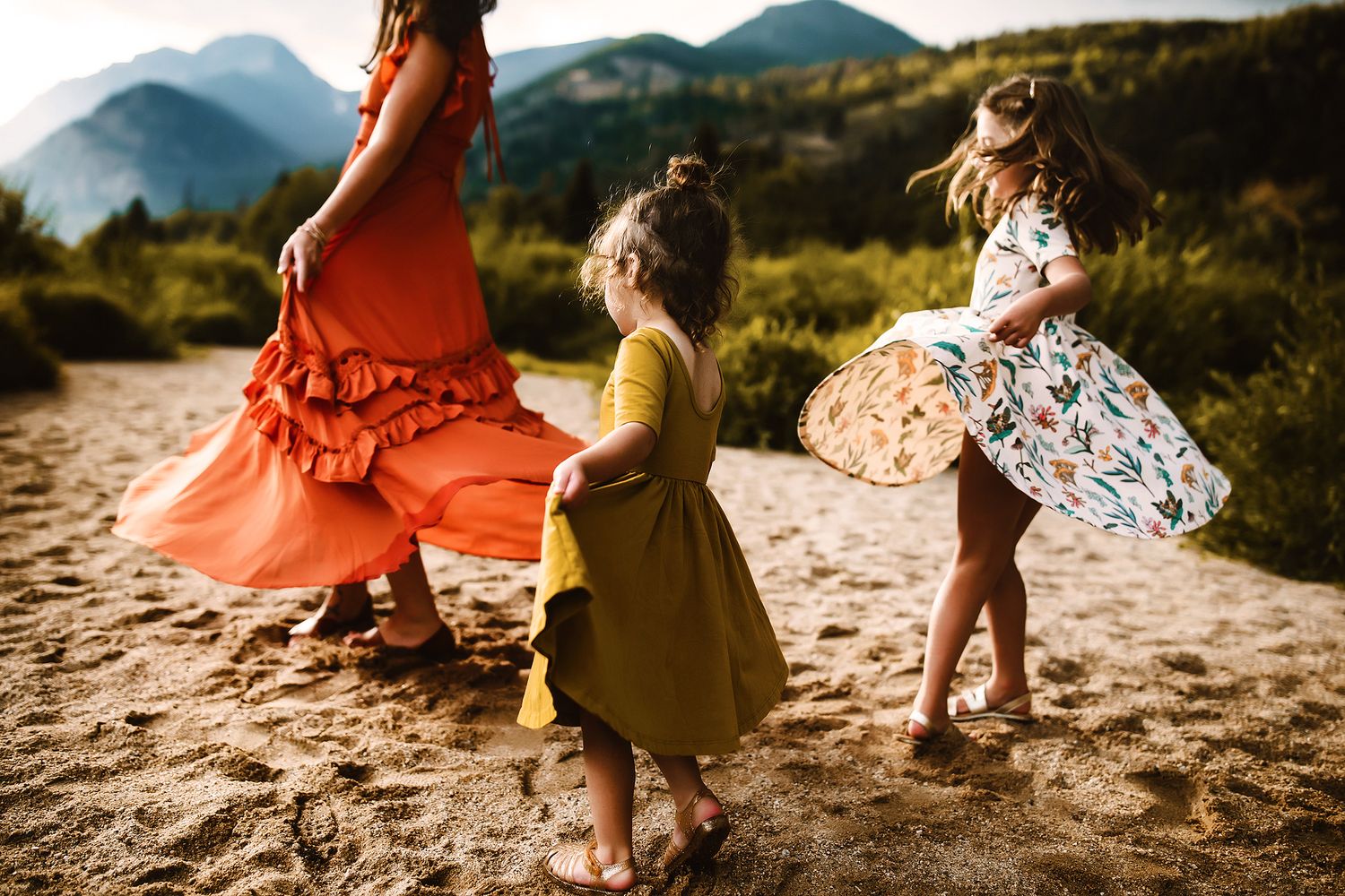 People walking on sandy mountain trail in colorful dresses during sunset.