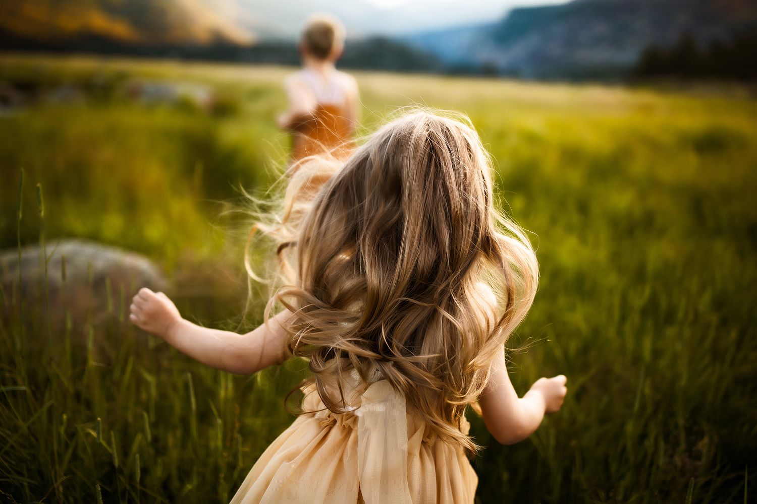 Person with flowing hair dances freely in a mountain meadow at sunset.