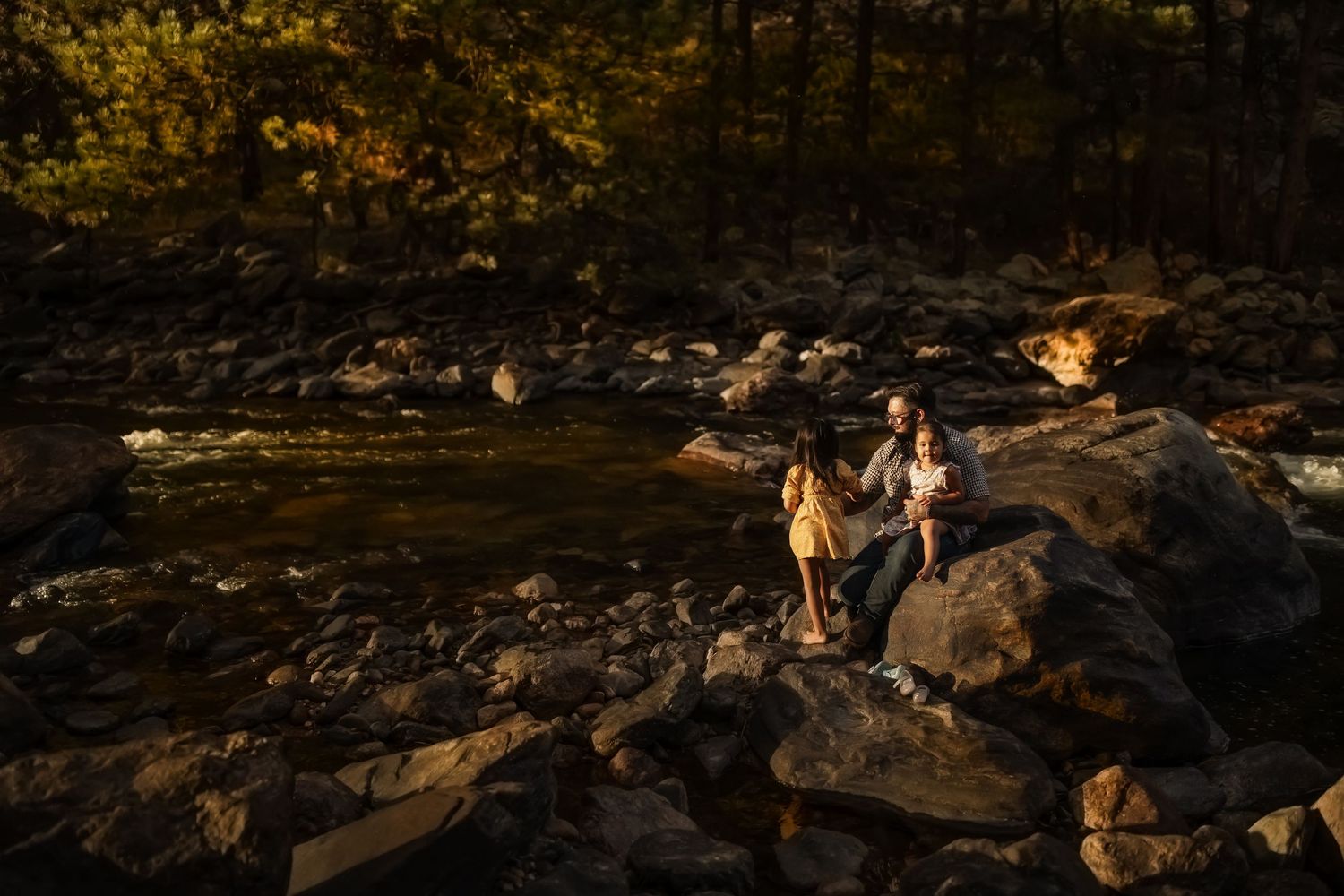 People walk along a rocky coastal shoreline during golden hour as sunlight casts warm shadows on the terrain.